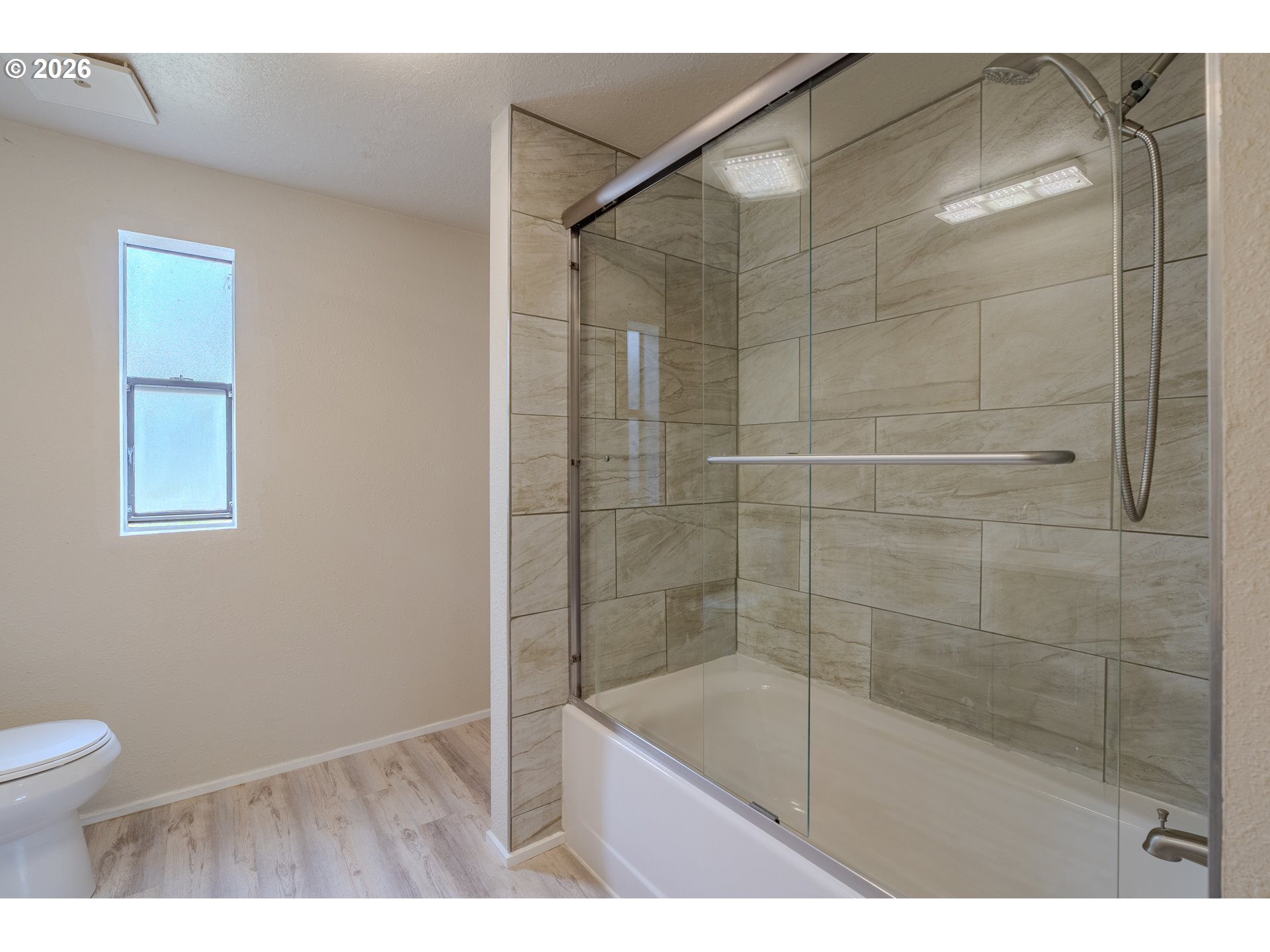 Bathroom with a glass shower enclosure, tiled walls, bathtub, and small window.