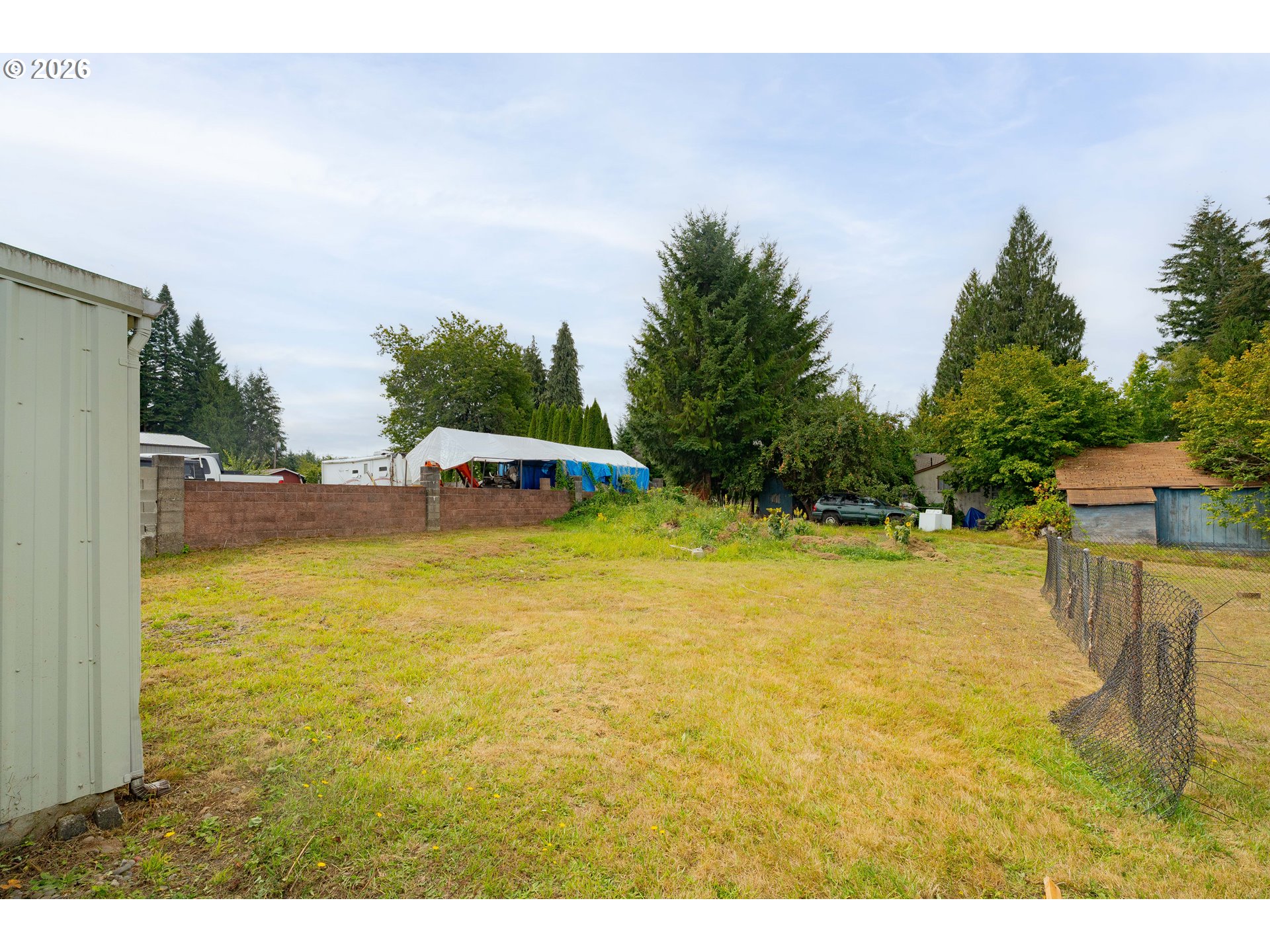 Open grassy backyard bordered by trees, with a low block wall and a loose chain-link fence.