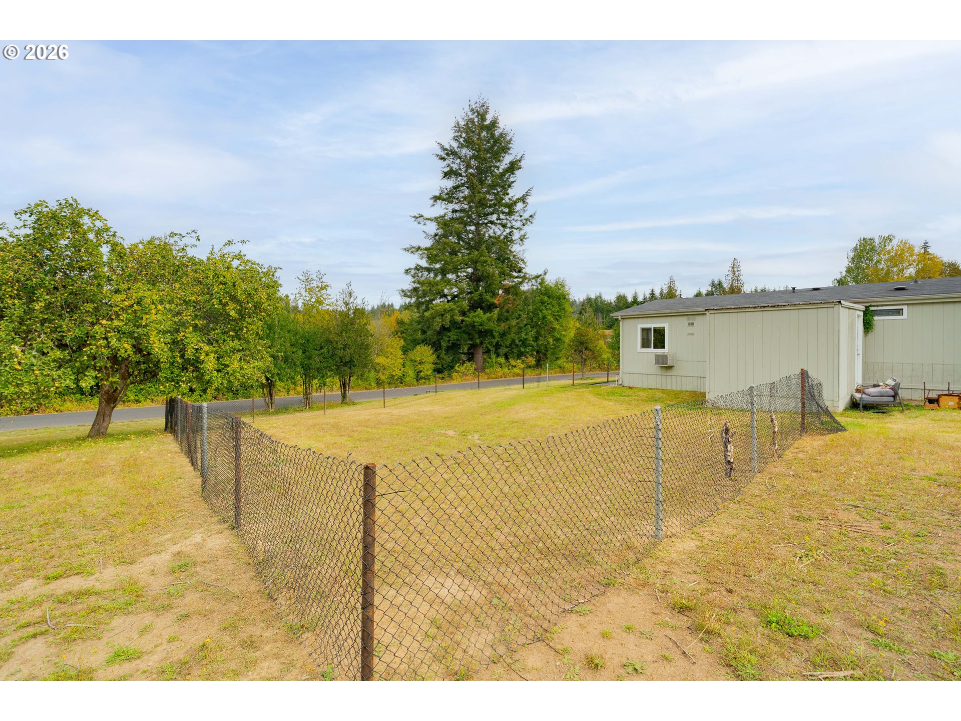 Light-colored home beside a chain-link-fenced yard with mature trees beyond.