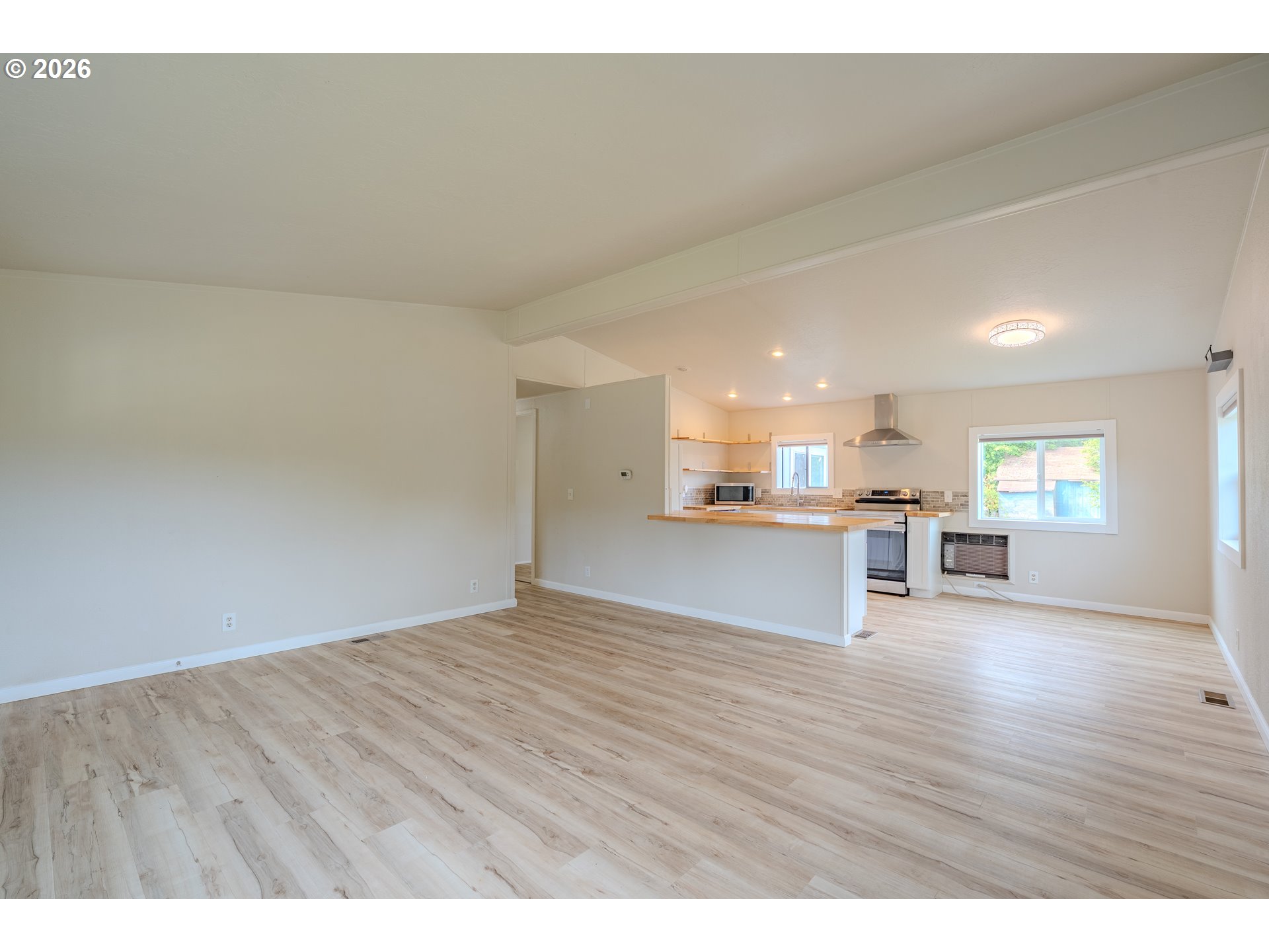 Vacant open-plan living area with light wood-look floors and an adjoining kitchen with a countertop peninsula.