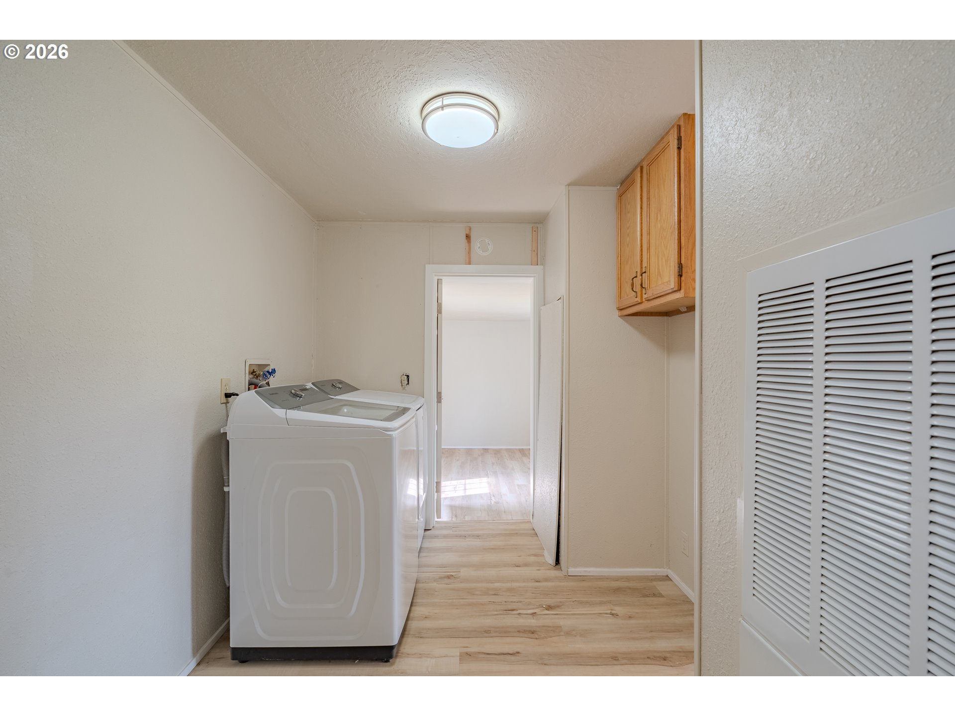 Laundry room with a top-loading washer, wood cabinet, and louvered closet doors.