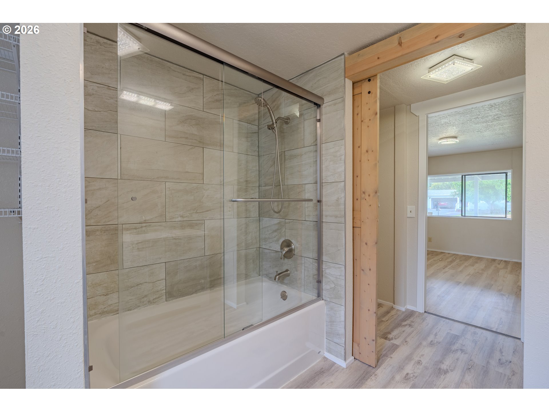 Bathroom with a glass-enclosed tiled tub and shower beside a wood-framed doorway.