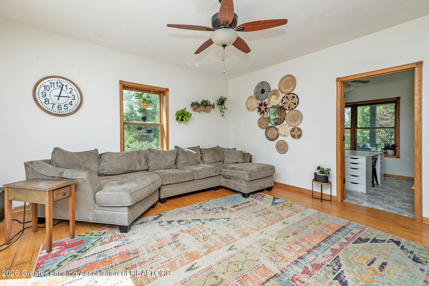 Living room with a gray sectional sofa, colorful patterned rug, and ceiling fan.