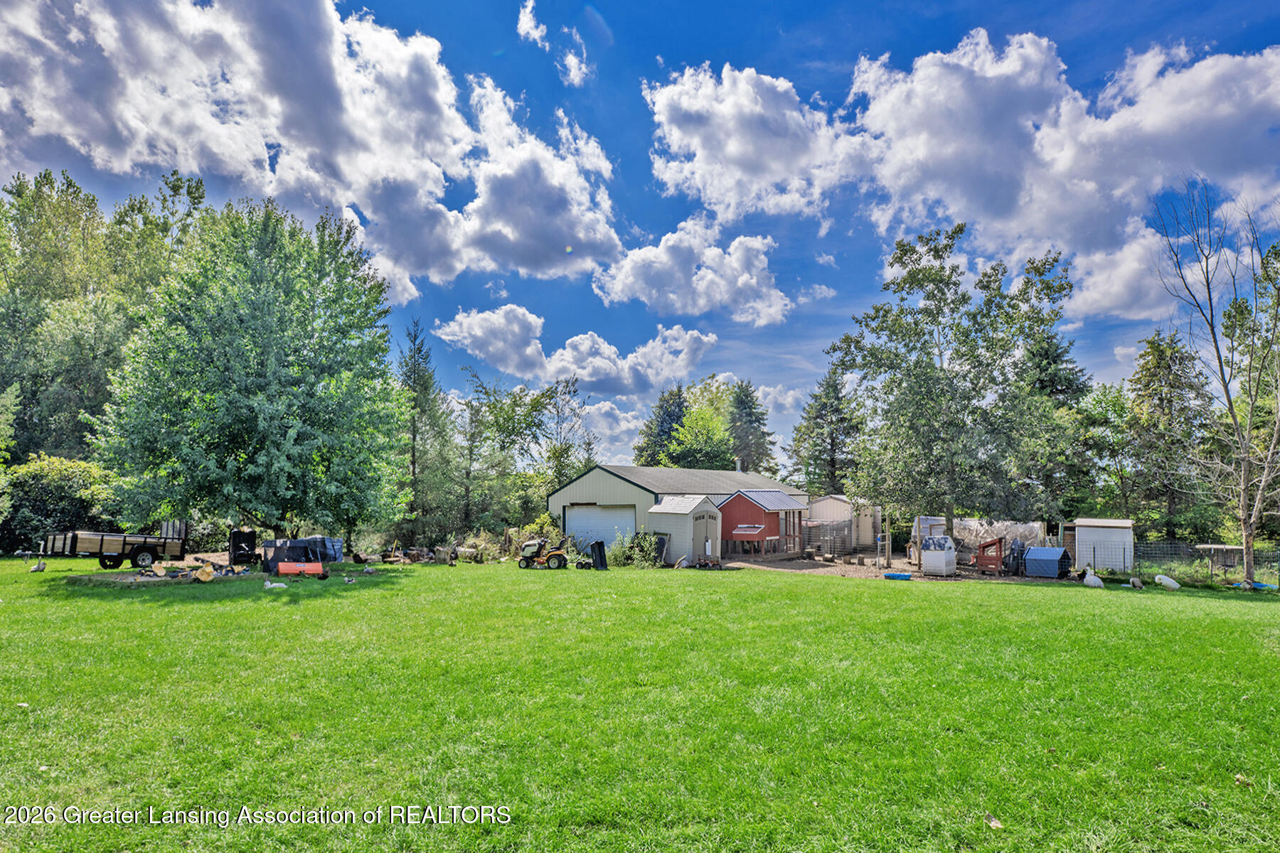 Lawn and detached garage buildings, including a red shed, beneath a blue sky with clouds.