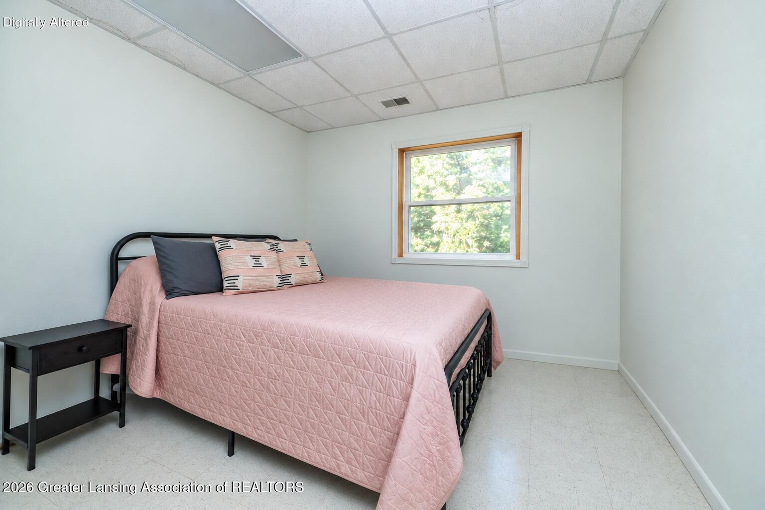 Bedroom with a pink-quilted bed, black metal frame, and window overlooking greenery.