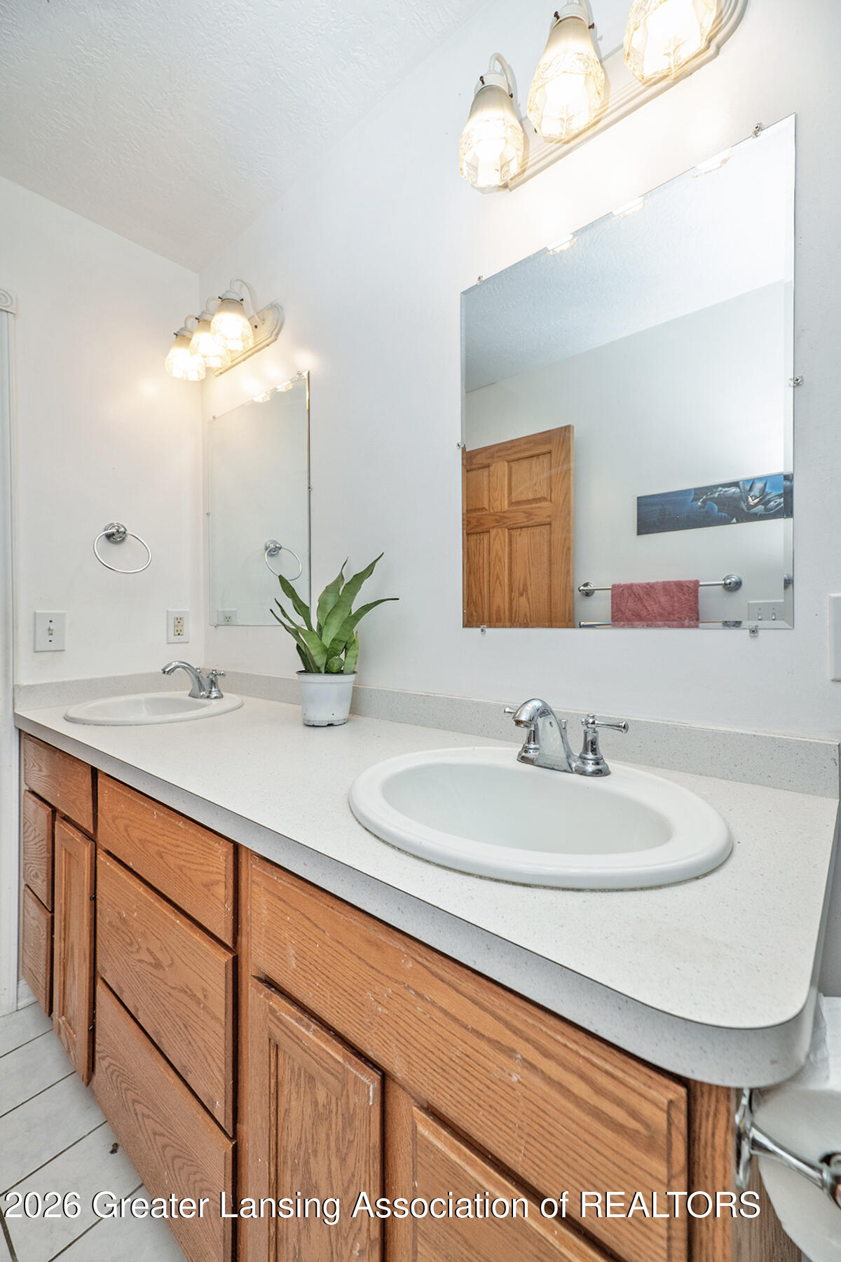 Bathroom vanity with two sinks, warm wood cabinets, large mirrors, and bright vanity lights.