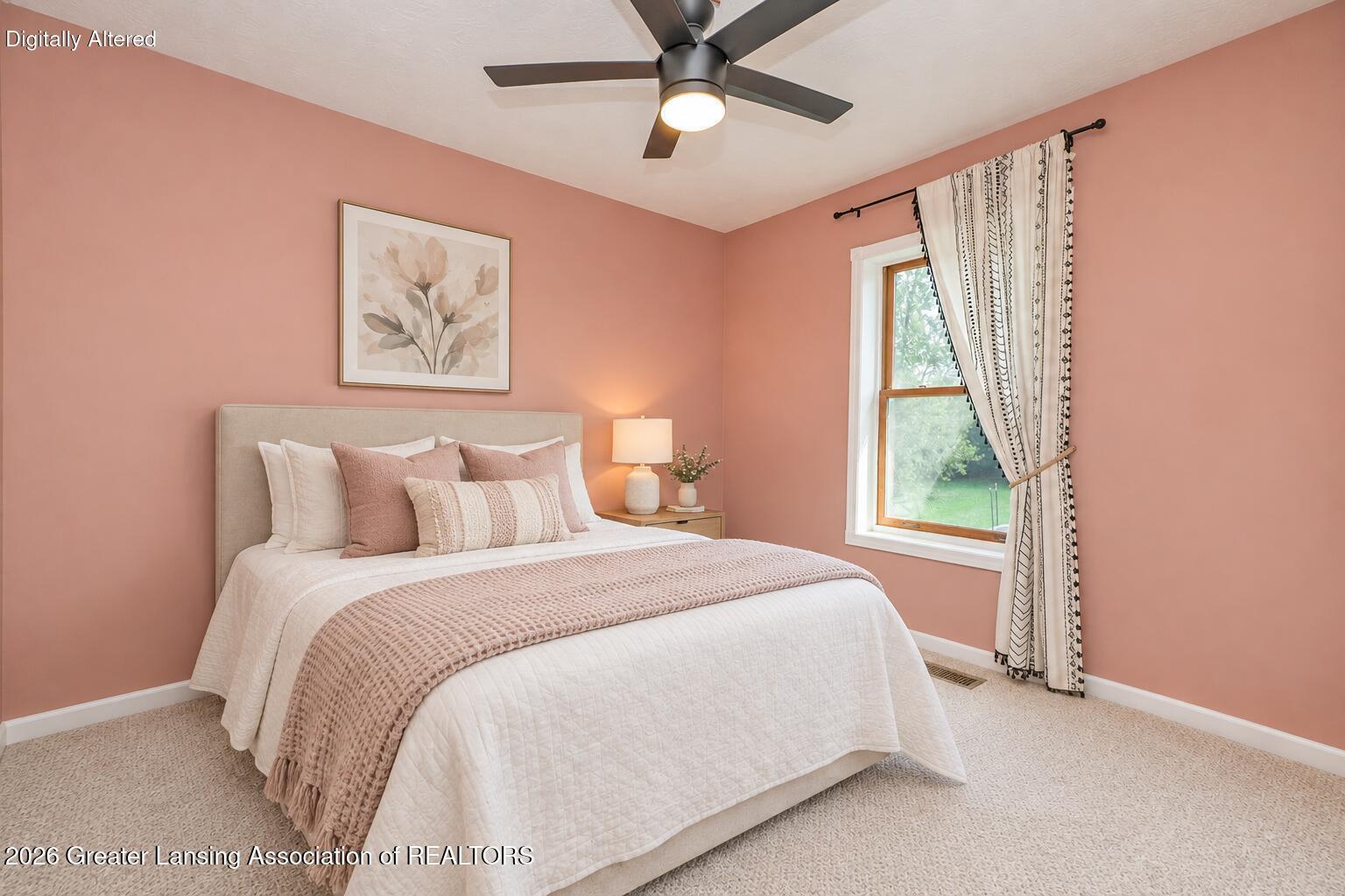 Staged bedroom with blush walls, a white bed, floral artwork, and a window overlooking greenery.