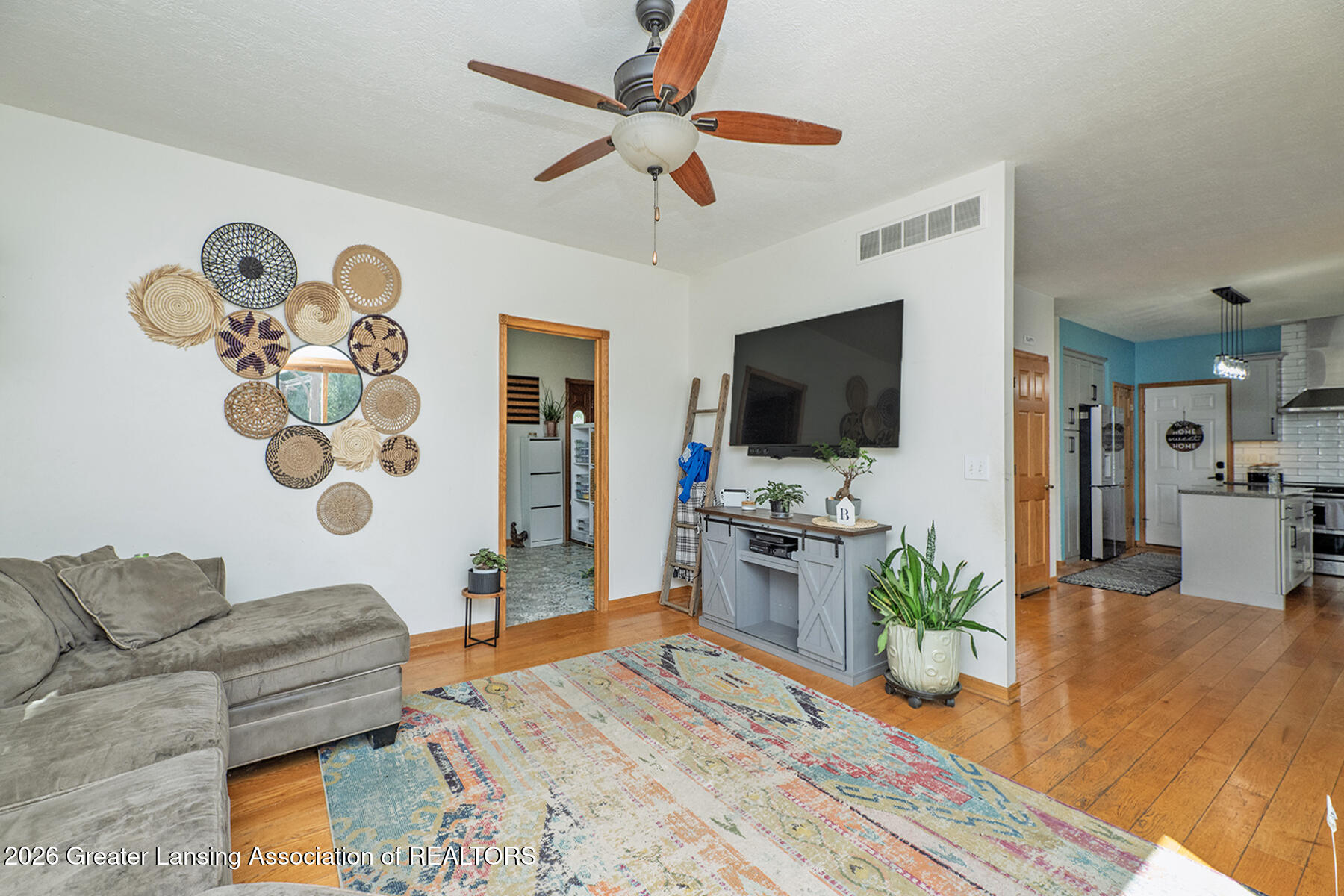 Living room with a gray sectional, colorful rug, hardwood floors, and wall-mounted television.