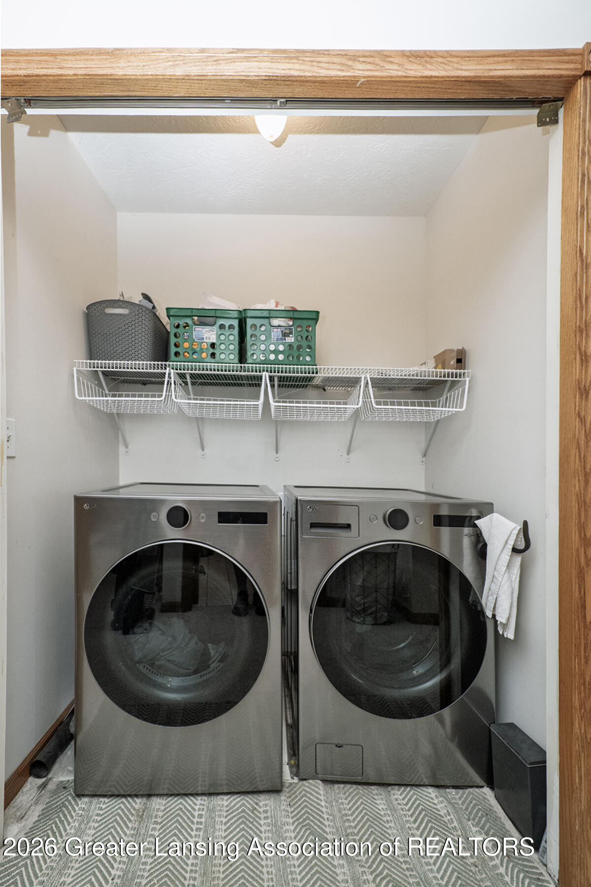 Laundry room with stainless-steel front-loading washer and dryer beneath storage shelves.