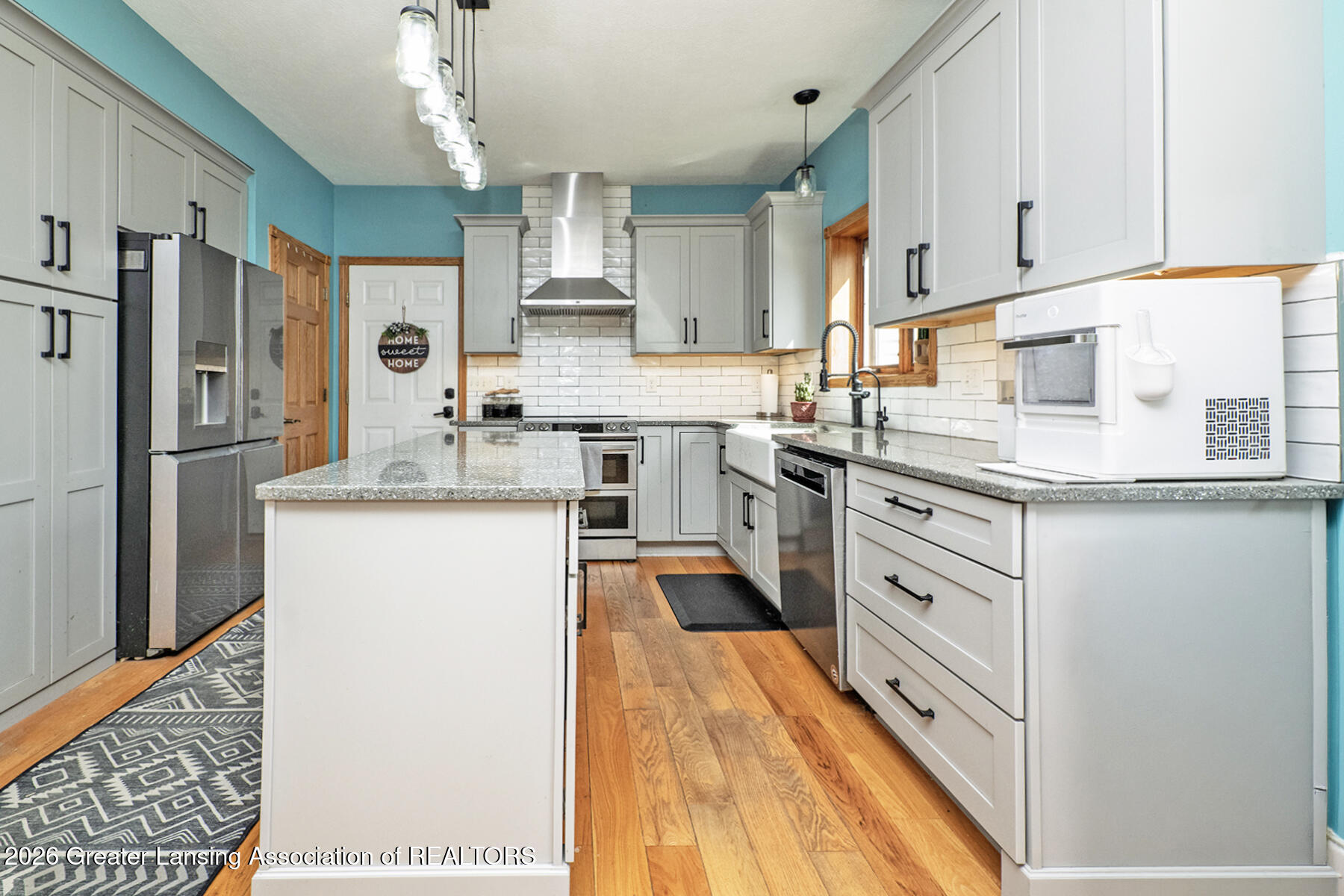 Remodeled kitchen with gray cabinets, turquoise walls, stainless appliances, and a large stone-topped island.