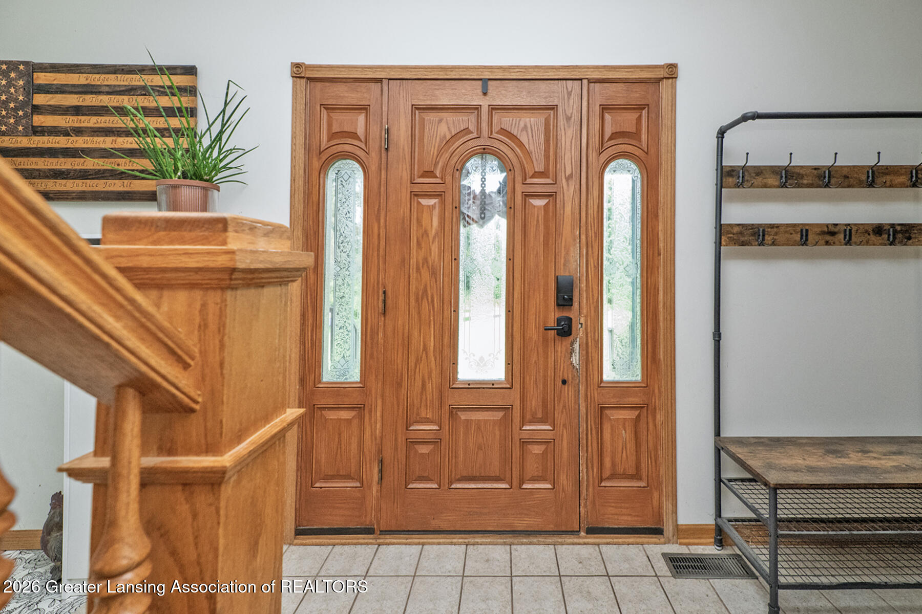 Entry foyer with ornate wooden front door, decorative glass sidelights, staircase, and tiled floor.
