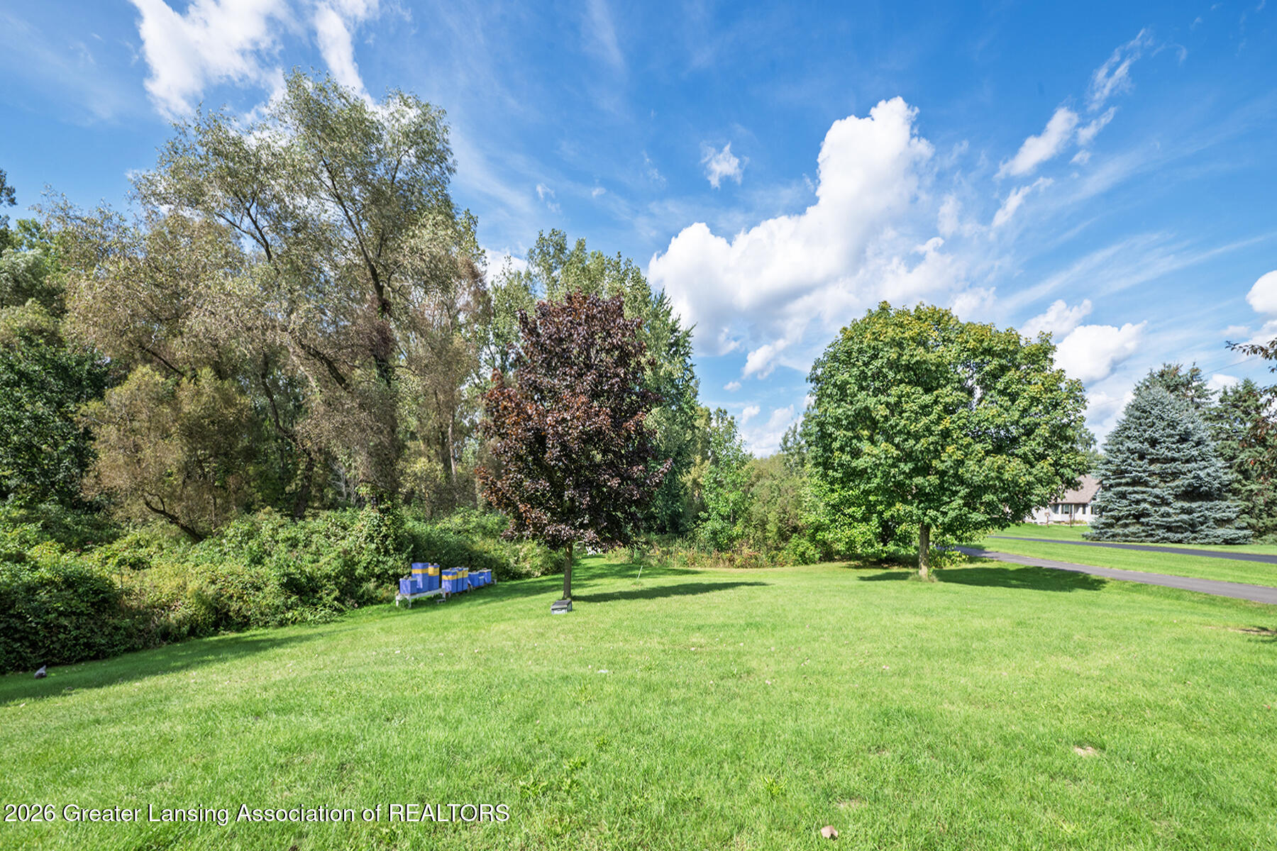 Landscaped property grounds with a broad lawn, mature trees, and beehive boxes.