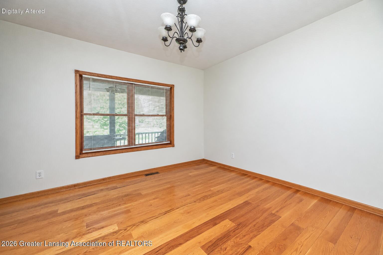 Empty room with polished hardwood floors, a large wood-trimmed window, and a chandelier.