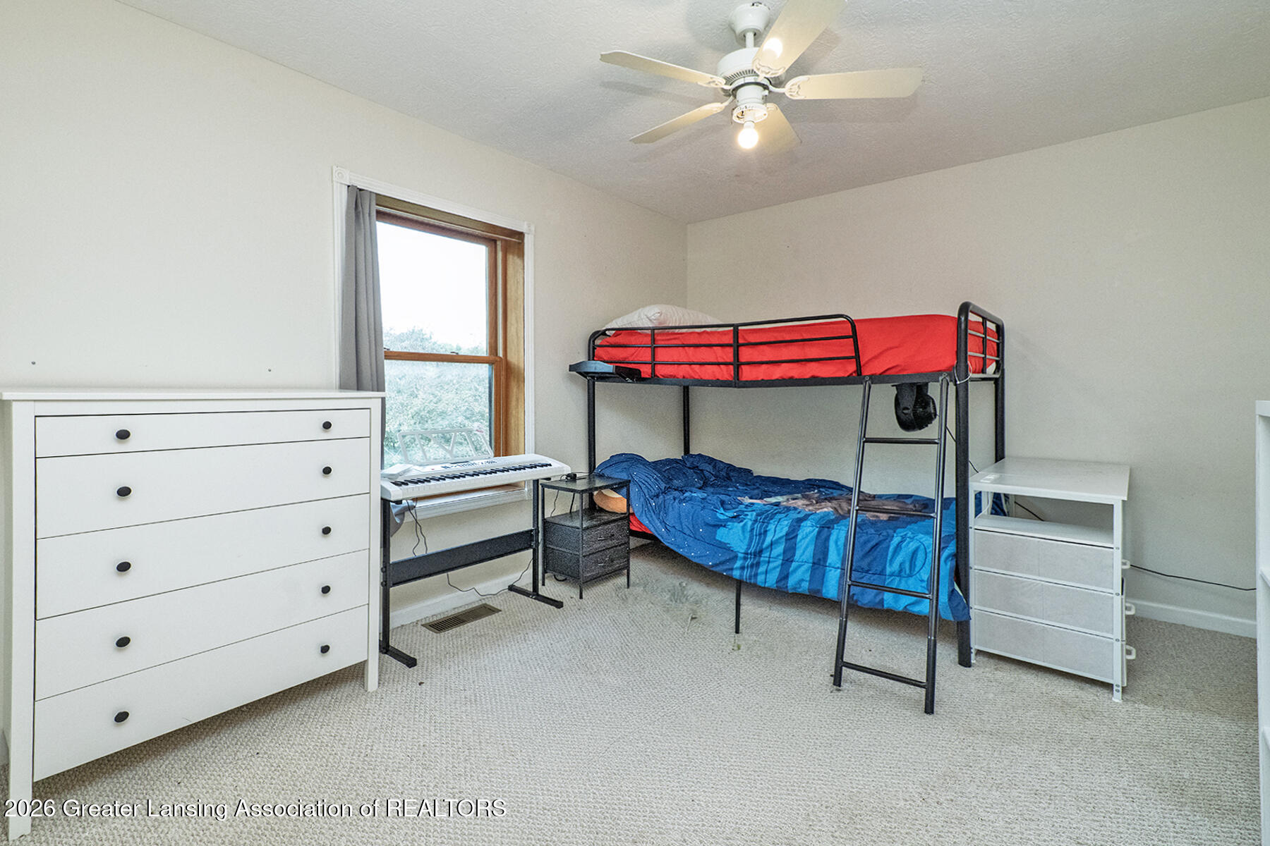 Bedroom with a black metal bunk bed, red upper mattress, blue bedding, and a keyboard beside the window.