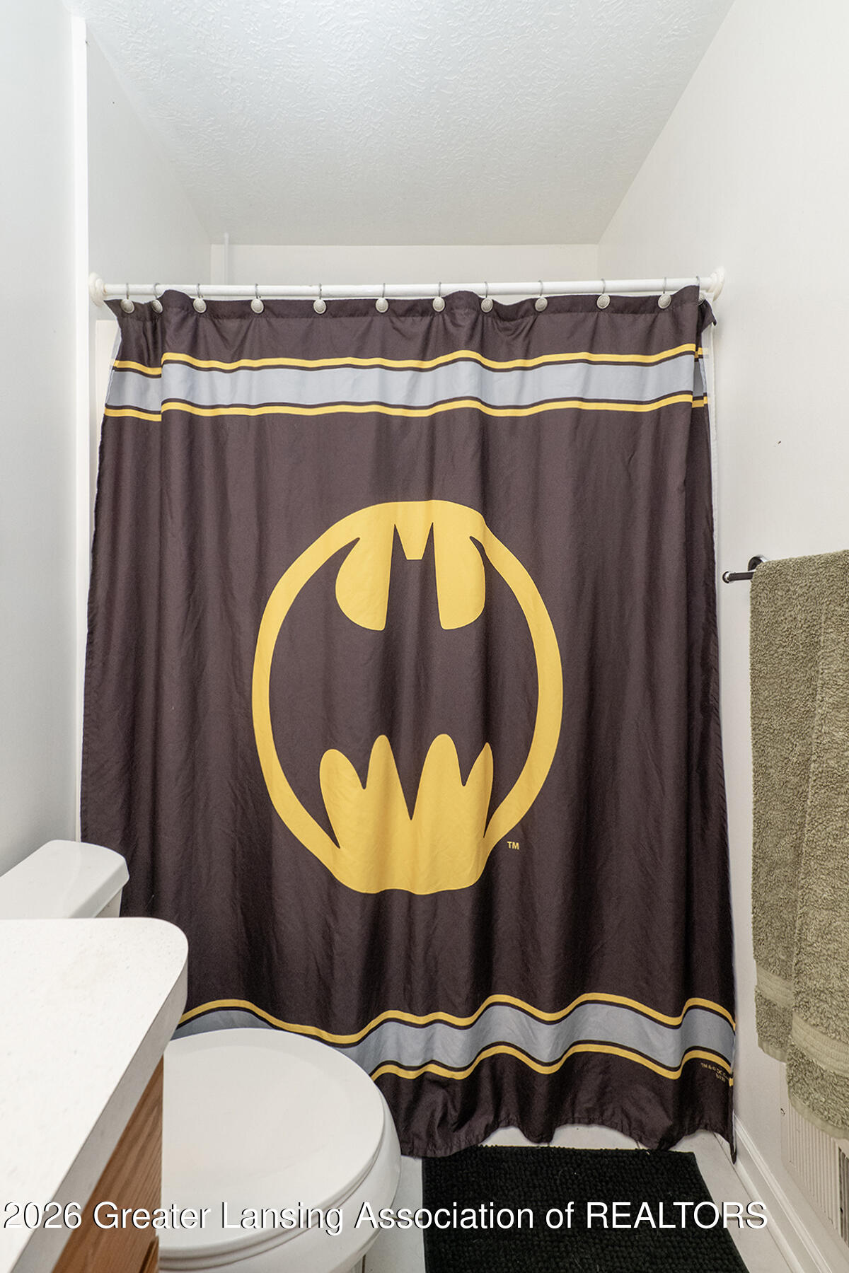 Bathroom with a Batman-logo shower curtain, white toilet, and green towel.