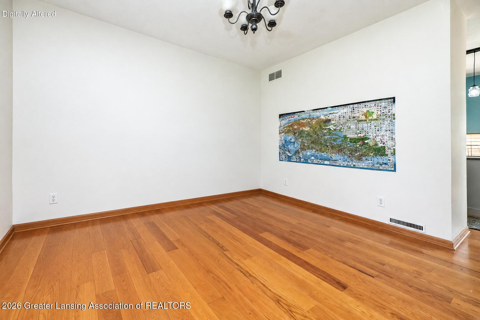Empty room with warm hardwood floors, a dark chandelier, and a large colorful wall hanging.
