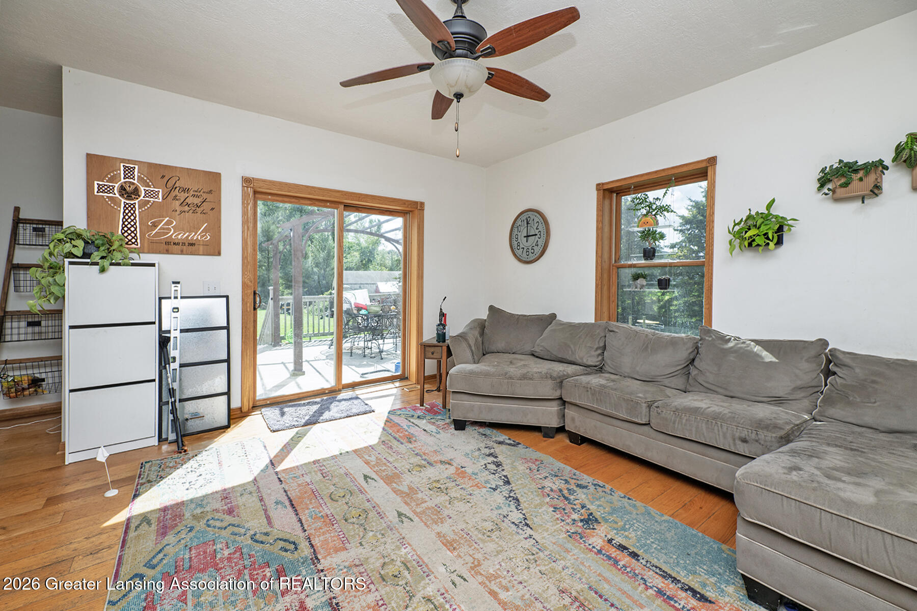 Living room with gray sectional, colorful rug, hardwood floors, and sliding glass door to a deck.