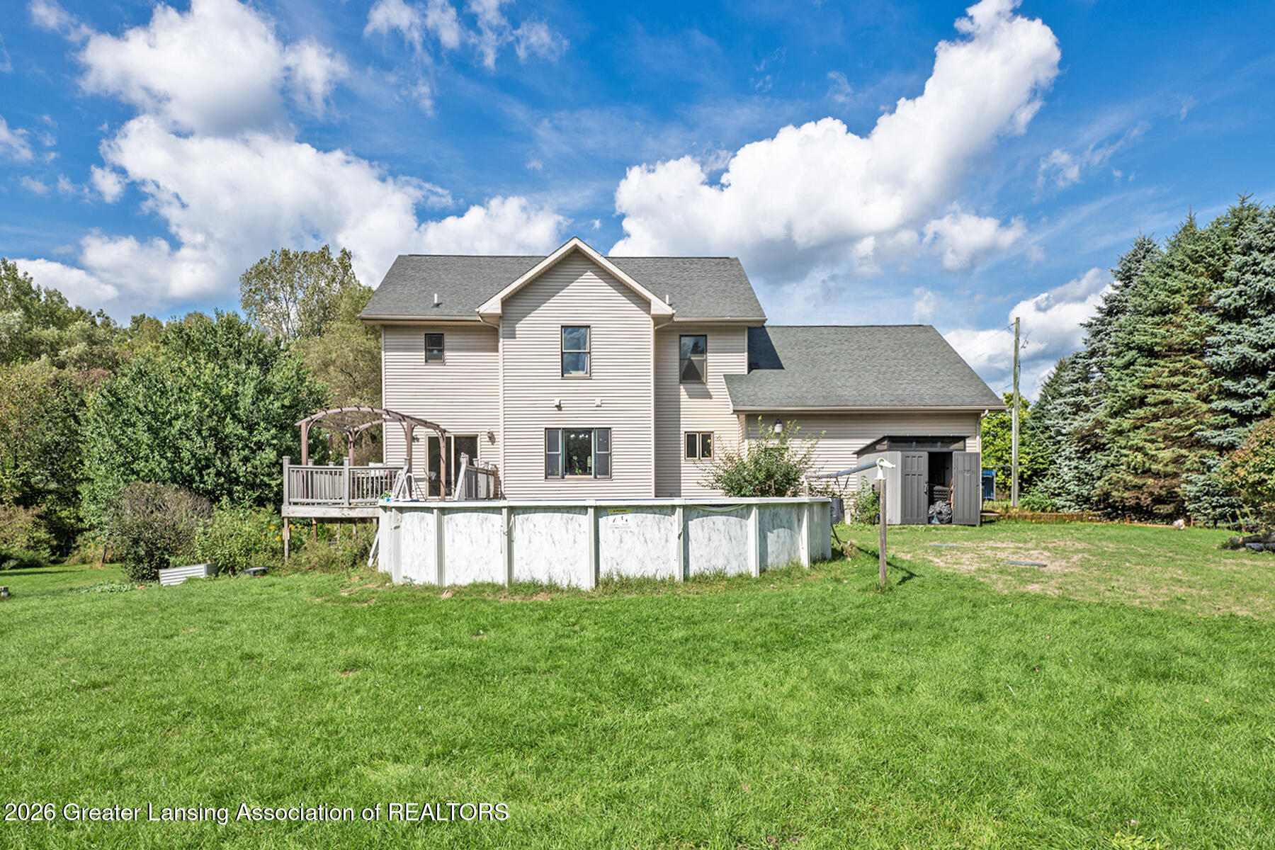 Rear of a two-story home with a raised deck, above-ground pool, and detached shed.