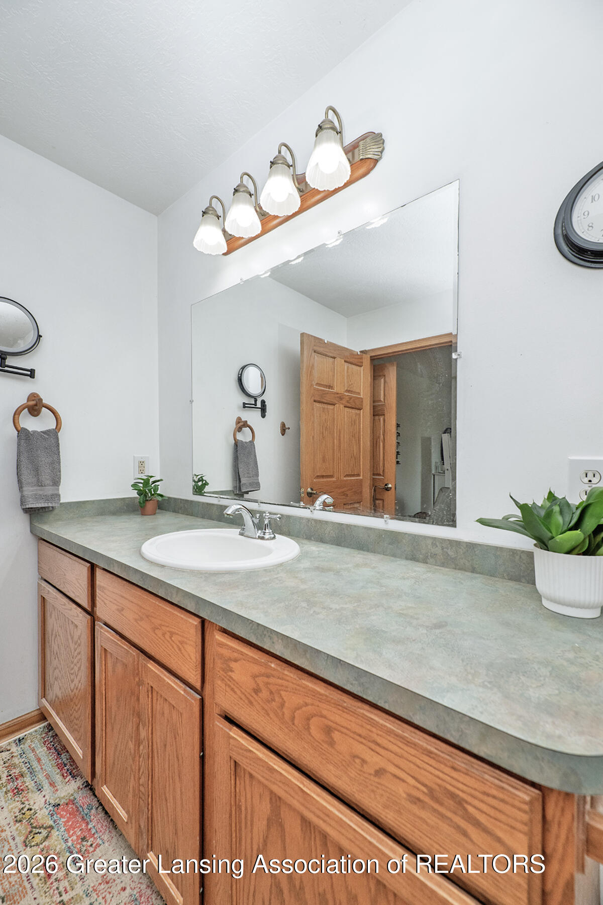 Bathroom vanity with a large mirror, green-gray countertop, white sink, and warm wood cabinets.