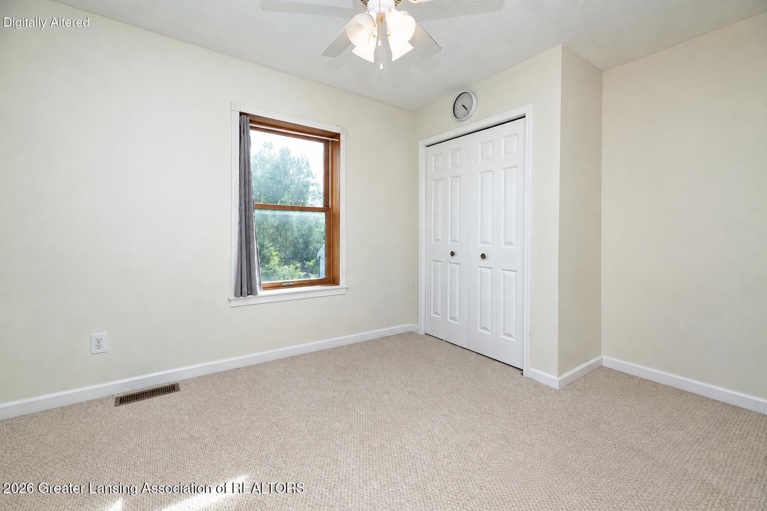 Empty carpeted bedroom with a wood-trimmed window, double closet doors, and ceiling fan.