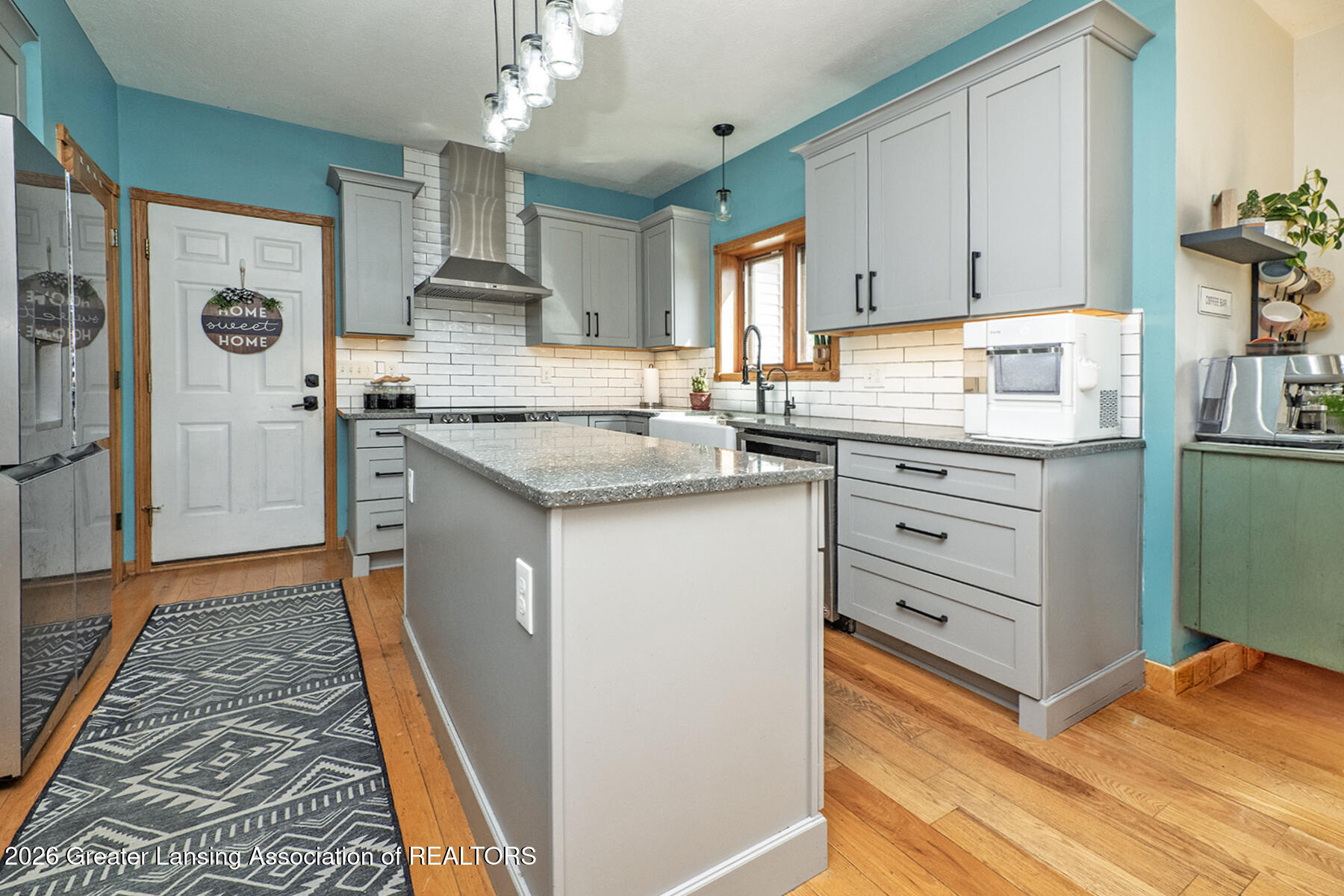 Kitchen with a large stone-topped island, gray cabinets, white subway tile, and teal walls.