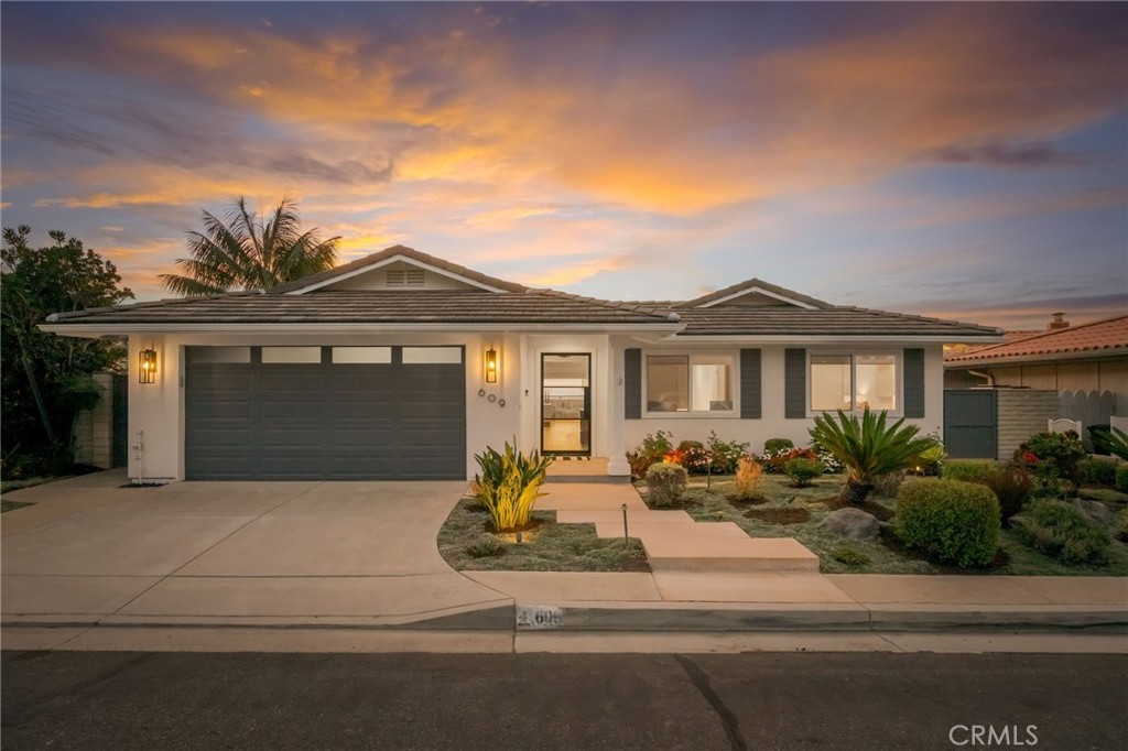 Single-story home with a dark double garage door and landscaped front yard at dusk.
