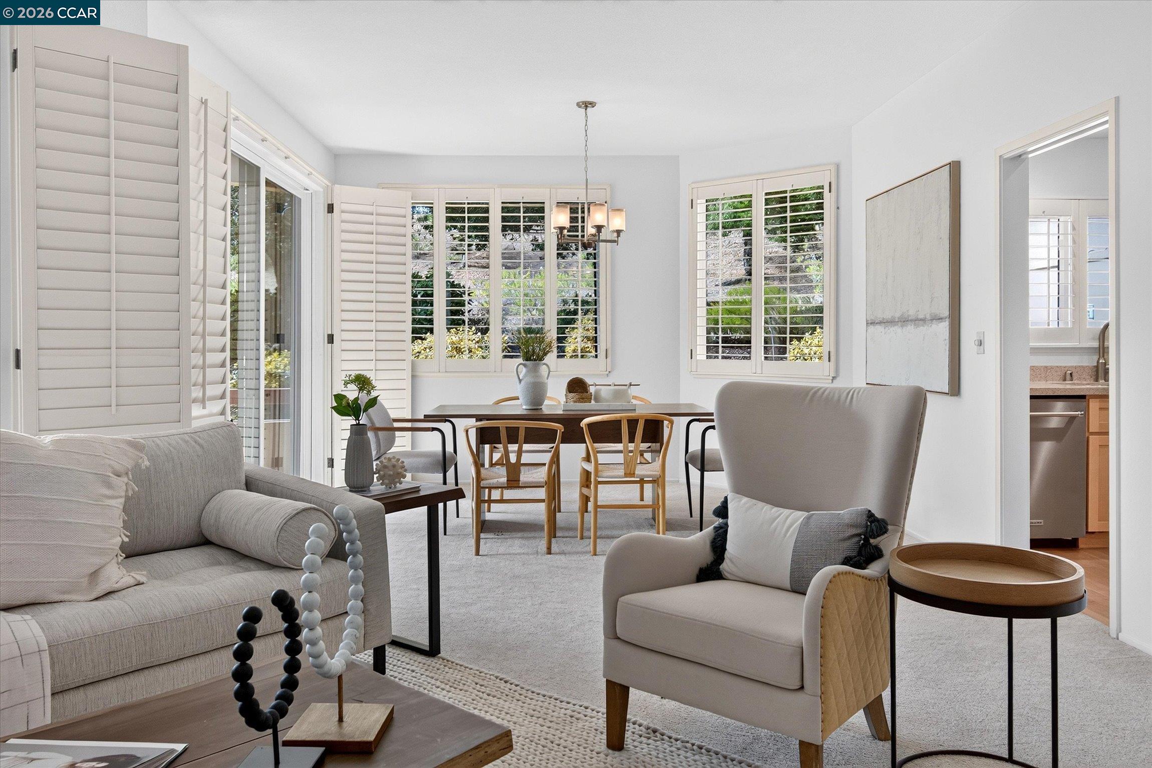 Living and dining room with plantation shutters, neutral seating, and an adjoining kitchen.