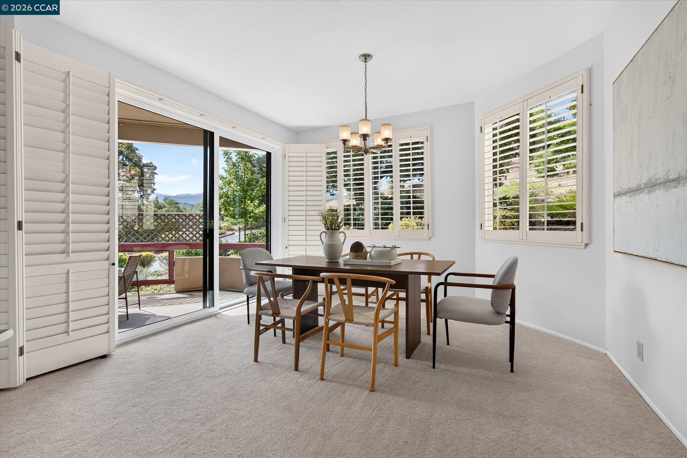 Dining room with plantation shutters, a chandelier, and sliding doors opening to a balcony.