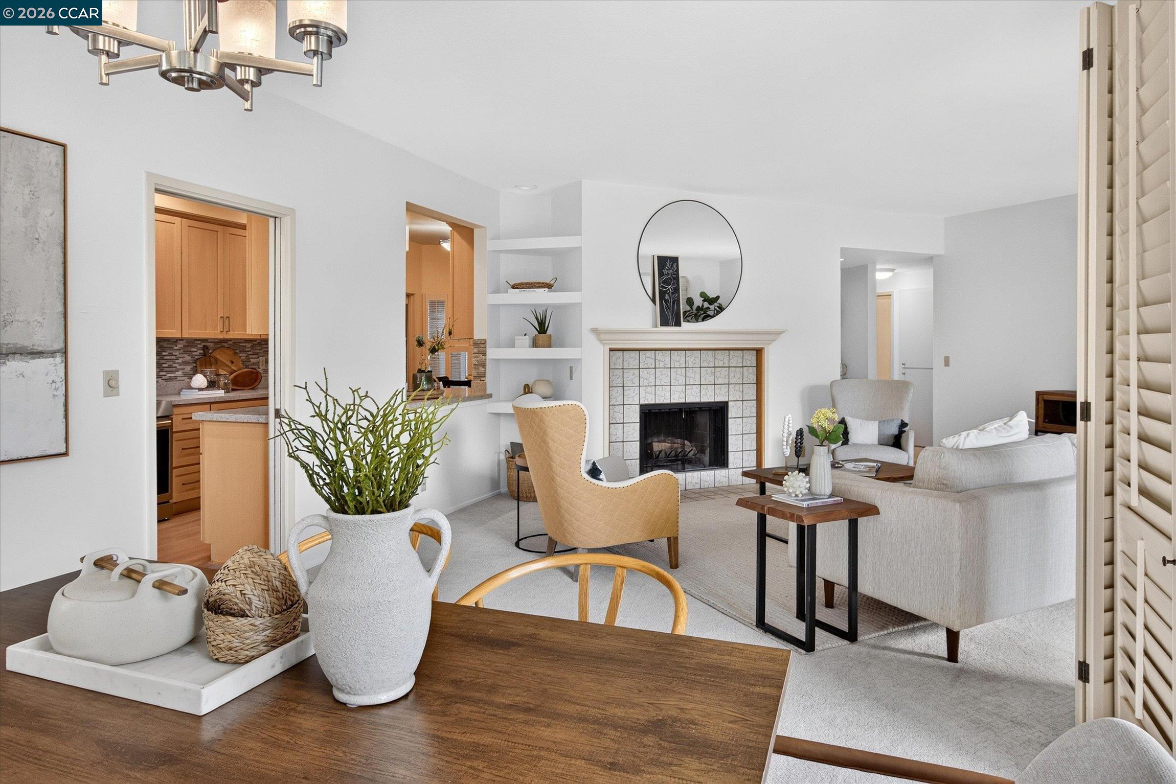 Staged living room with a tiled fireplace, built-in shelves, and an open view into the kitchen.