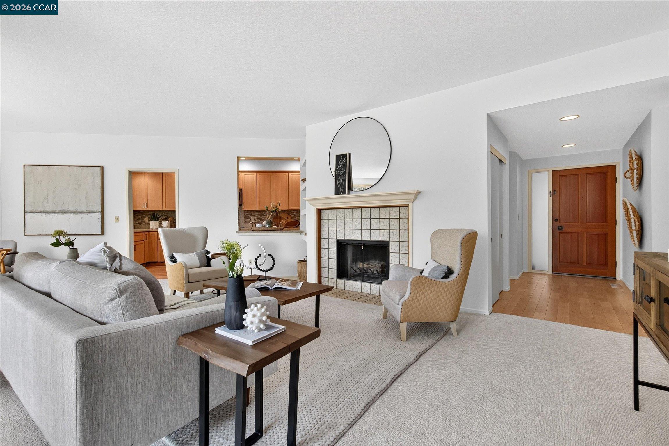 Staged living room with a tiled fireplace, gray sectional, and open kitchen.