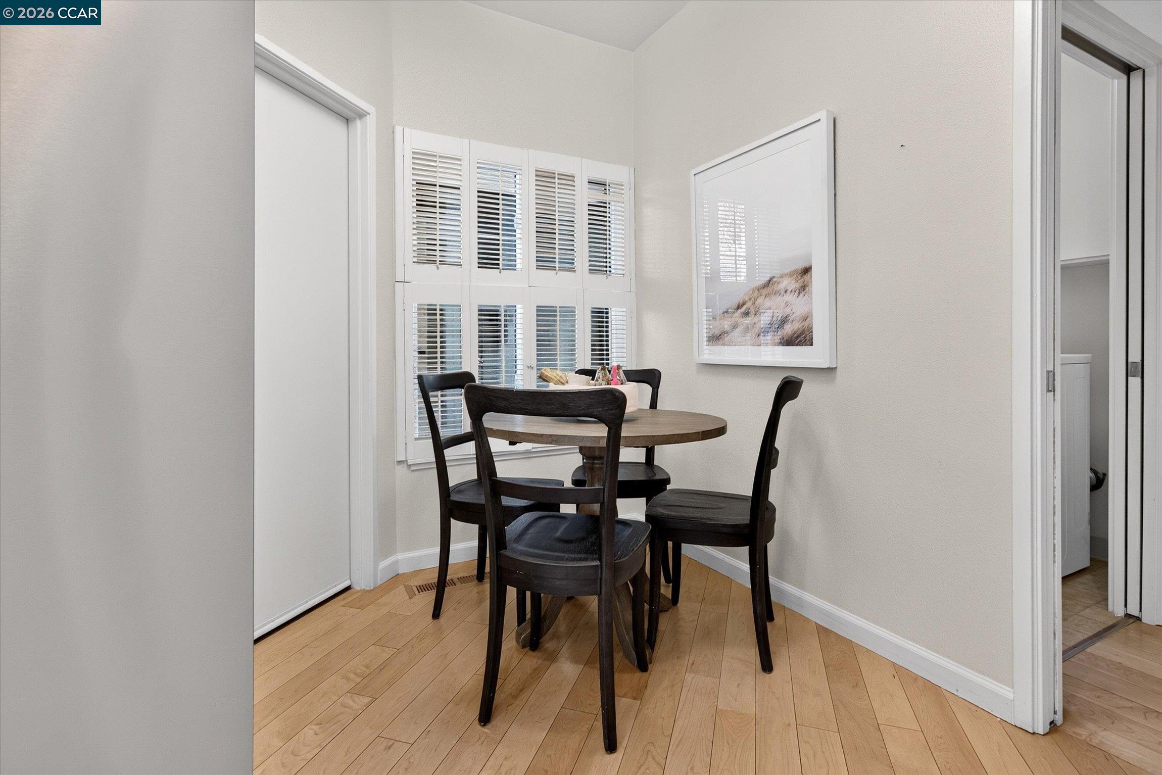 Dining nook with a round table, dark chairs, plantation shutters, and hardwood floors.