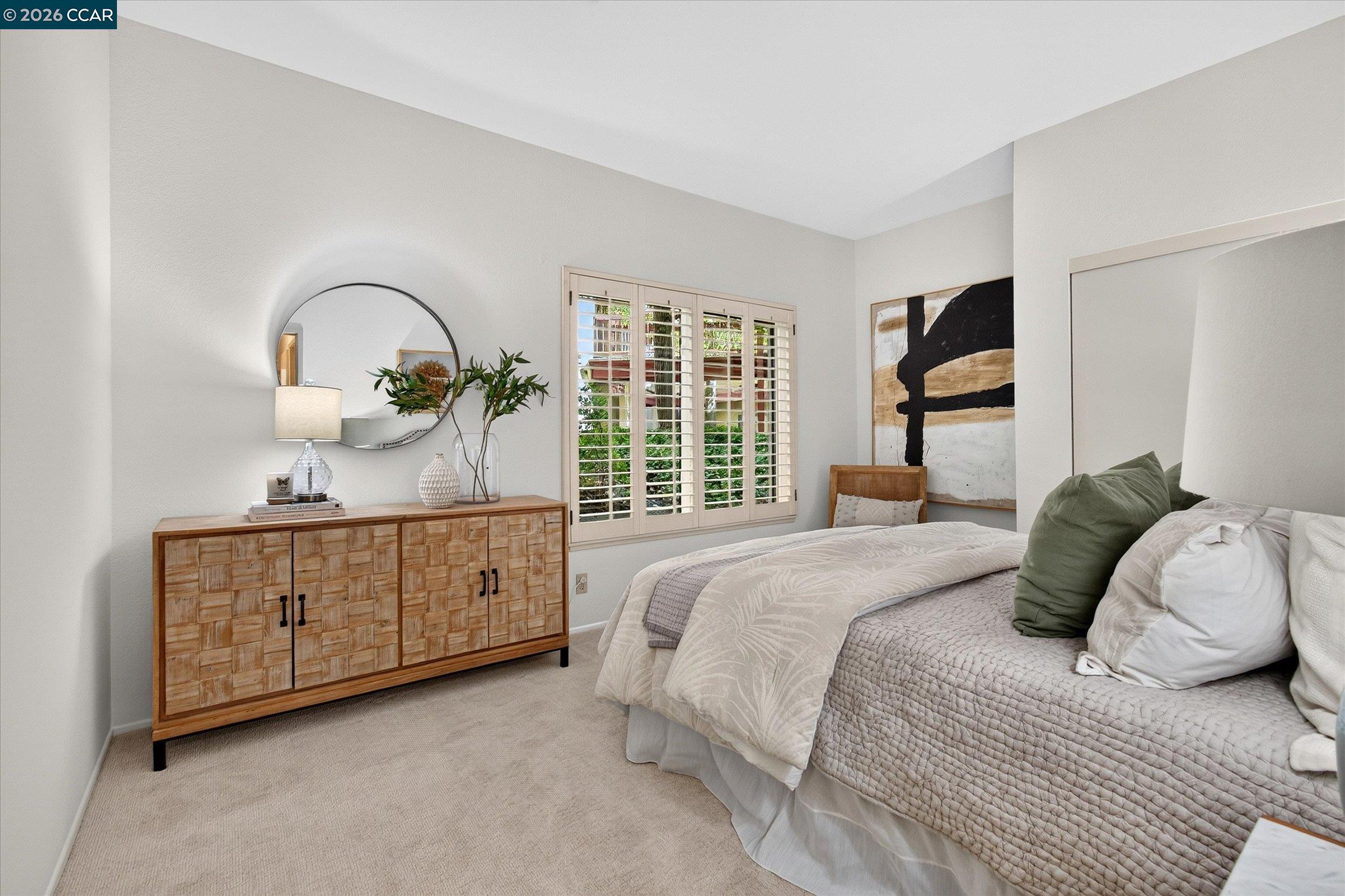 Furnished bedroom with a large neutral-toned bed, wood sideboard, and shuttered windows.
