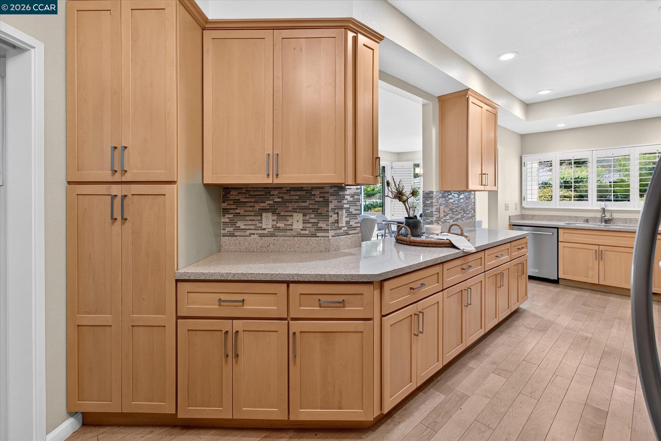 Kitchen with a large wood-cabinet island, mosaic backsplash, and plantation-shuttered windows.