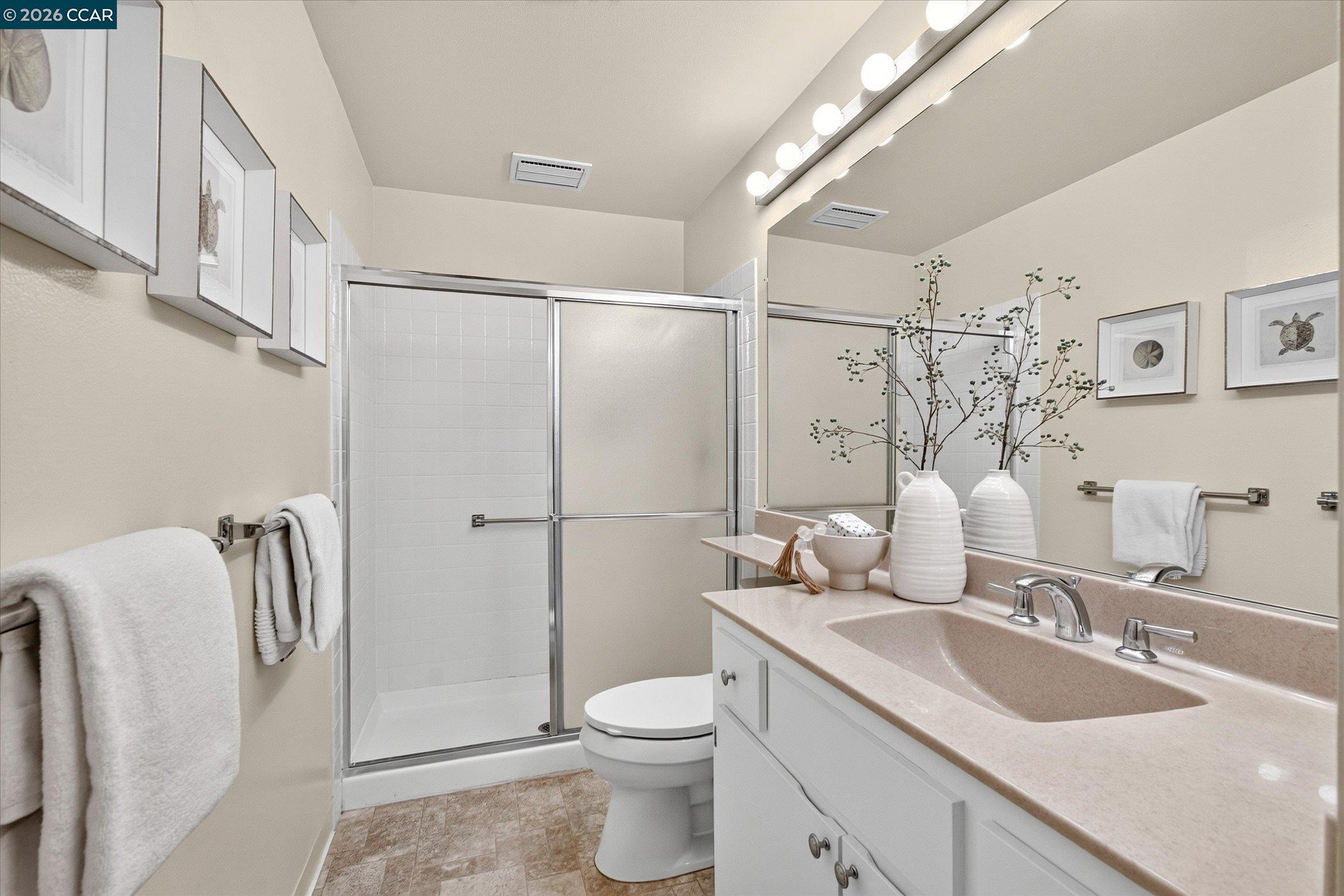 Bathroom with a glass-enclosed shower, pale vanity, large mirror, and framed coastal artwork.