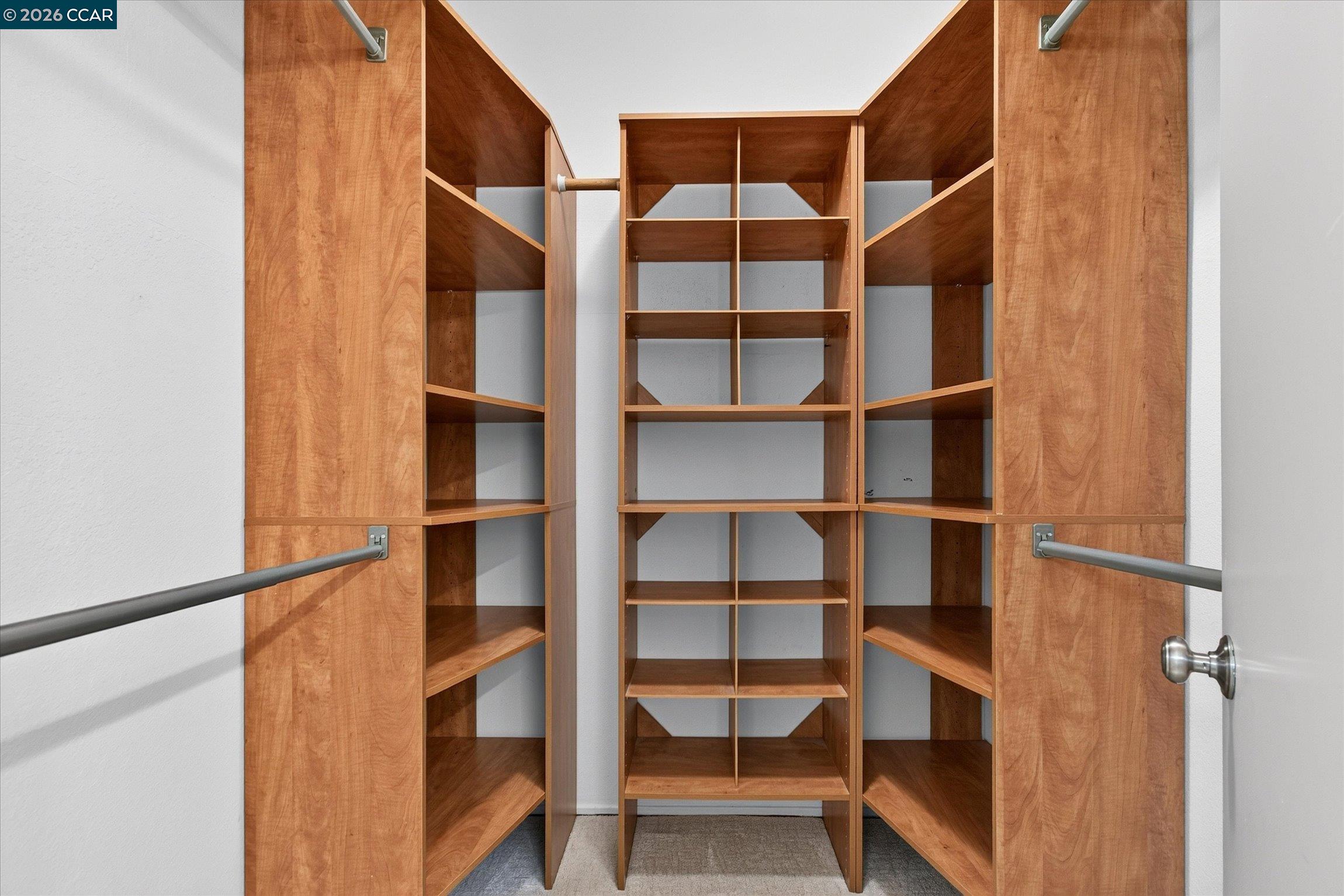 Walk-in closet with extensive empty wooden shelving and hanging rods.