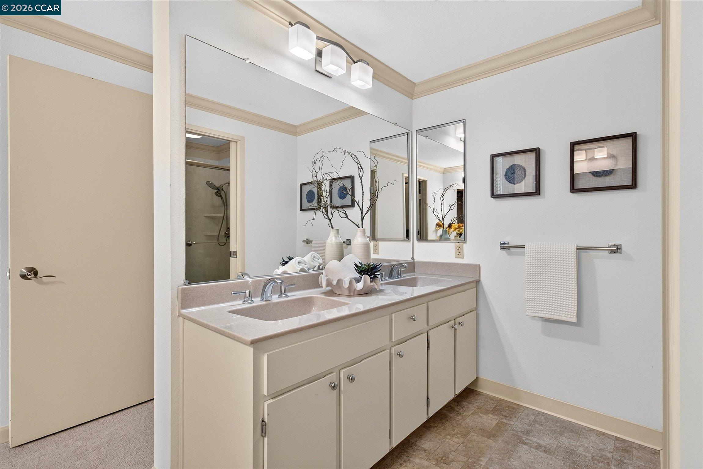 Bathroom with a double-sink vanity, two mirrors, and a shower visible through the doorway.