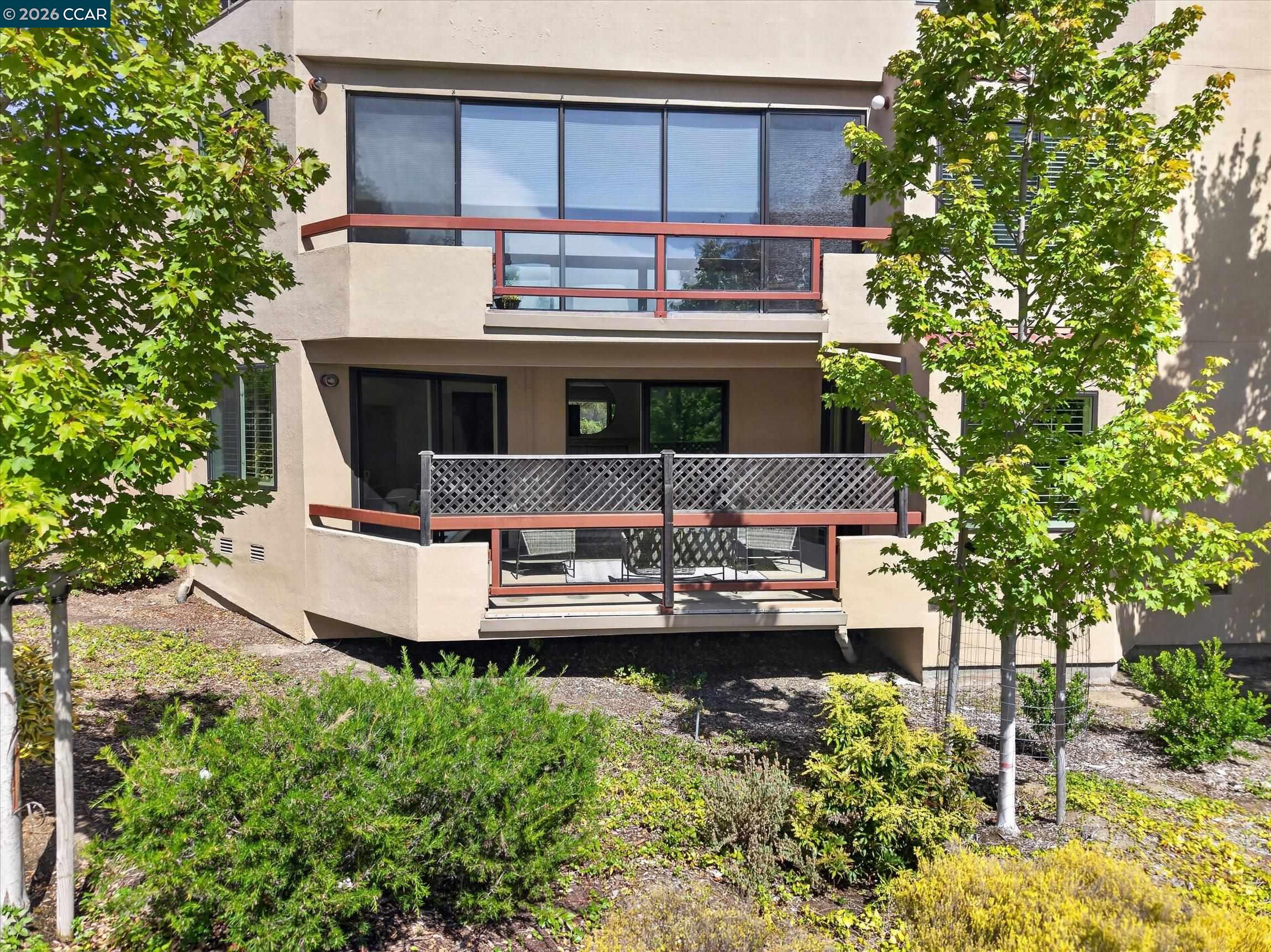 Condominium exterior with two balconies, patio seating, and landscaped grounds.