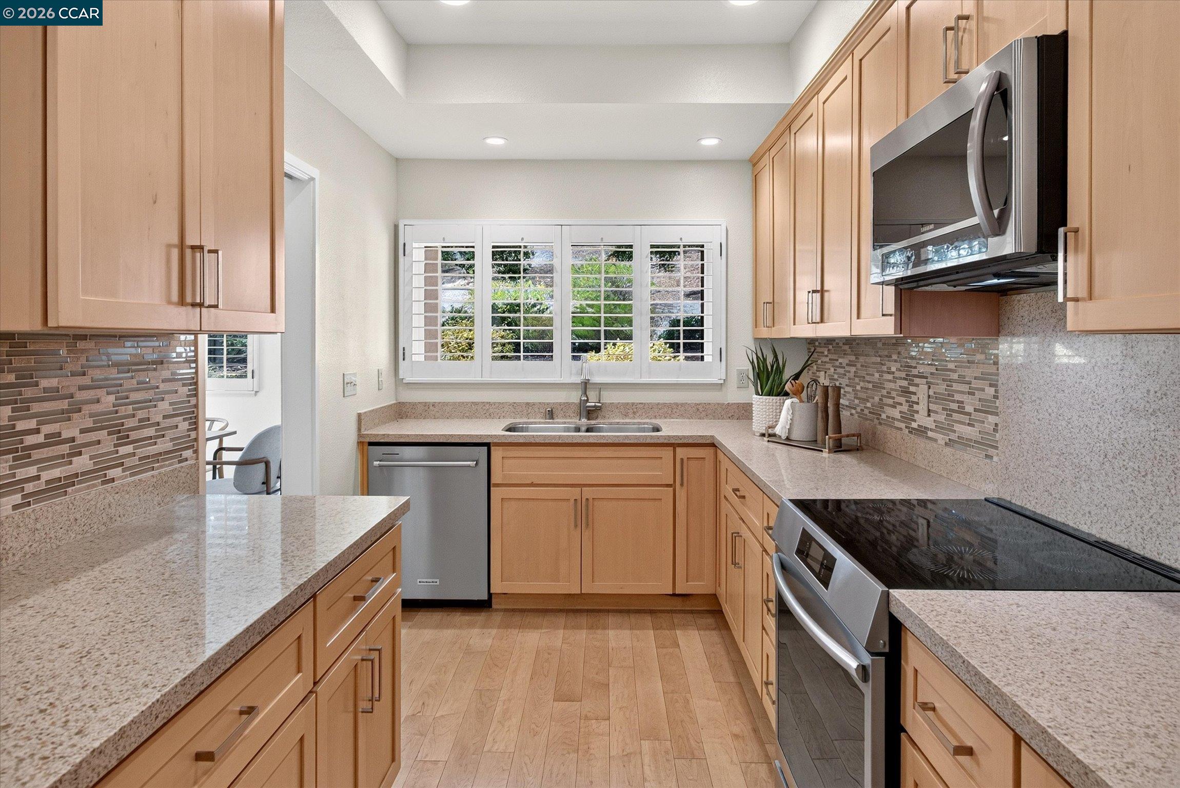 Kitchen with light wood cabinets, stone counters, mosaic backsplash, and stainless steel appliances.