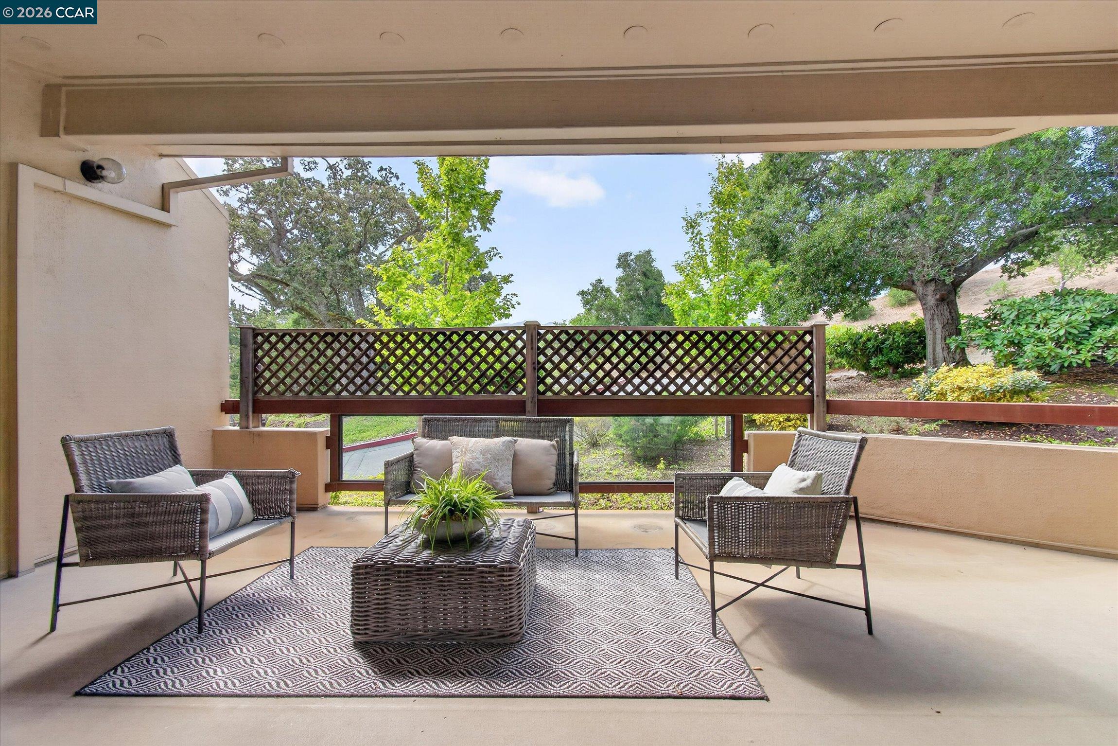 Covered patio with wicker seating, a patterned rug, and a view of trees.