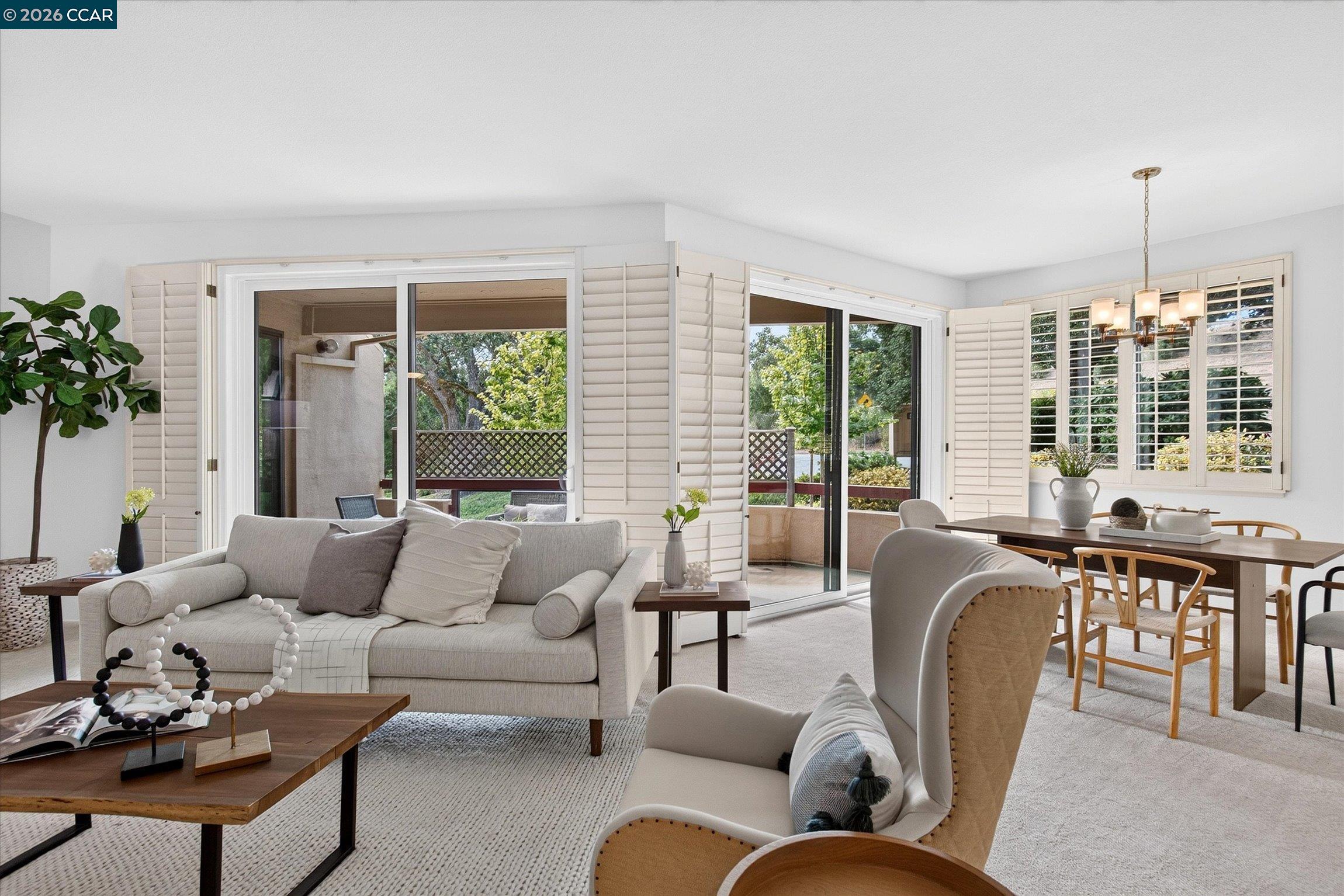 Living and dining room with plantation shutters and sliding doors opening to a leafy patio.