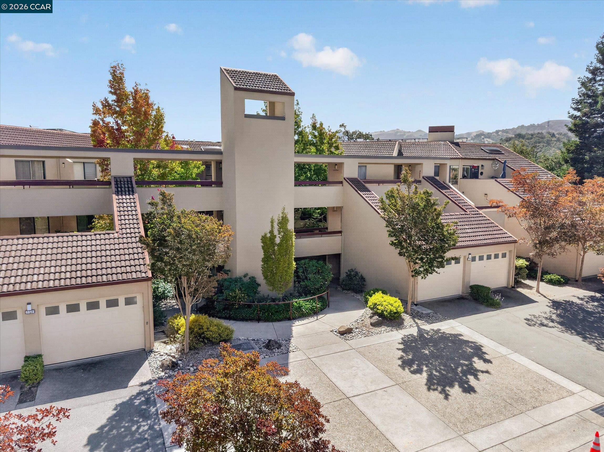 Multi-unit residence with tiled roofs, garages, landscaped walkways, and a central tower.