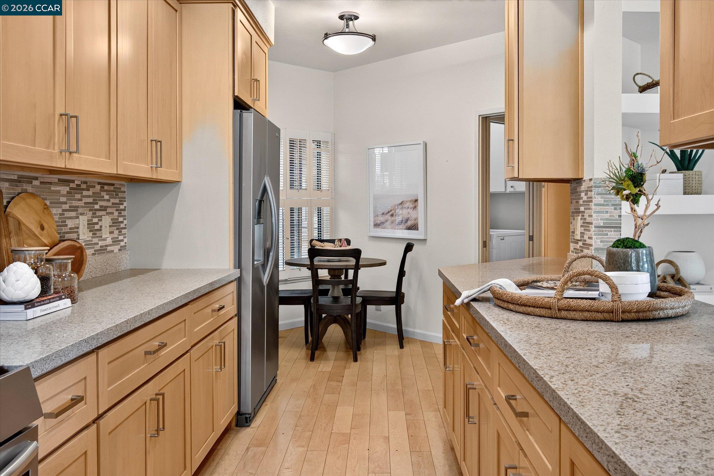 Kitchen with light wood cabinets, granite countertops, and a dining nook beside shuttered windows.