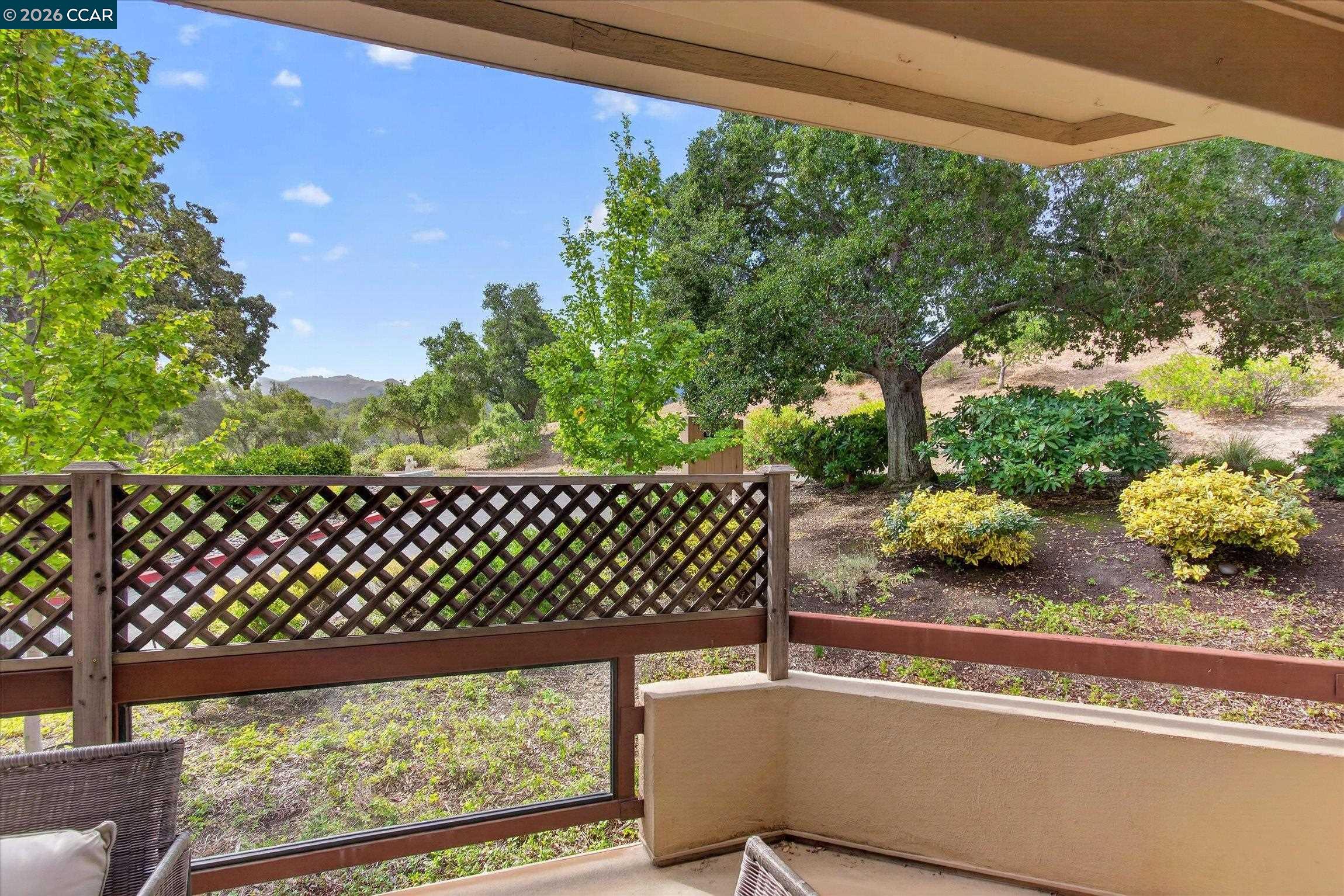Covered patio overlooking a landscaped hillside, with a lattice railing and outdoor seating.