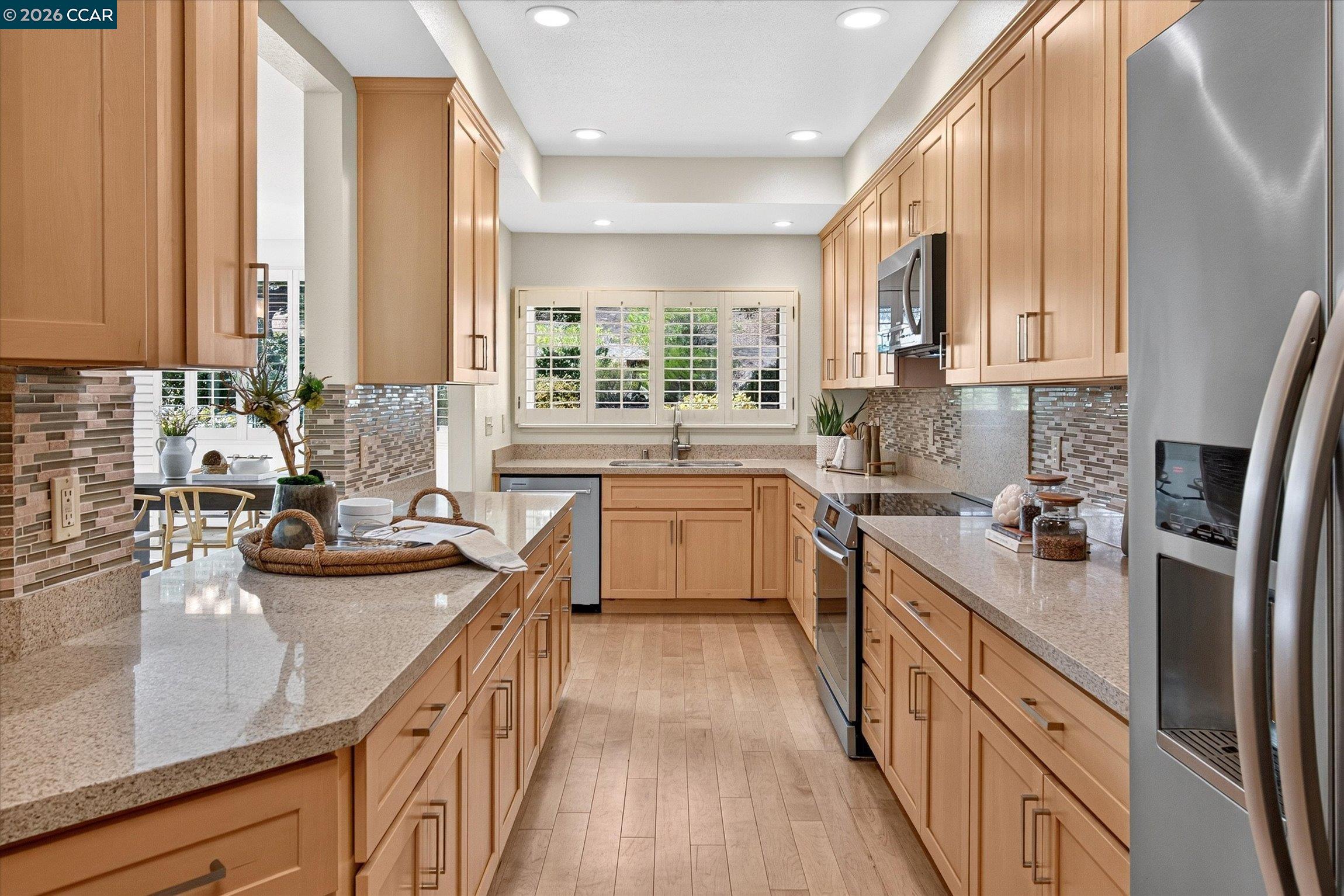 Kitchen with light wood cabinets, stone island countertop, stainless steel appliances, and shuttered windows.