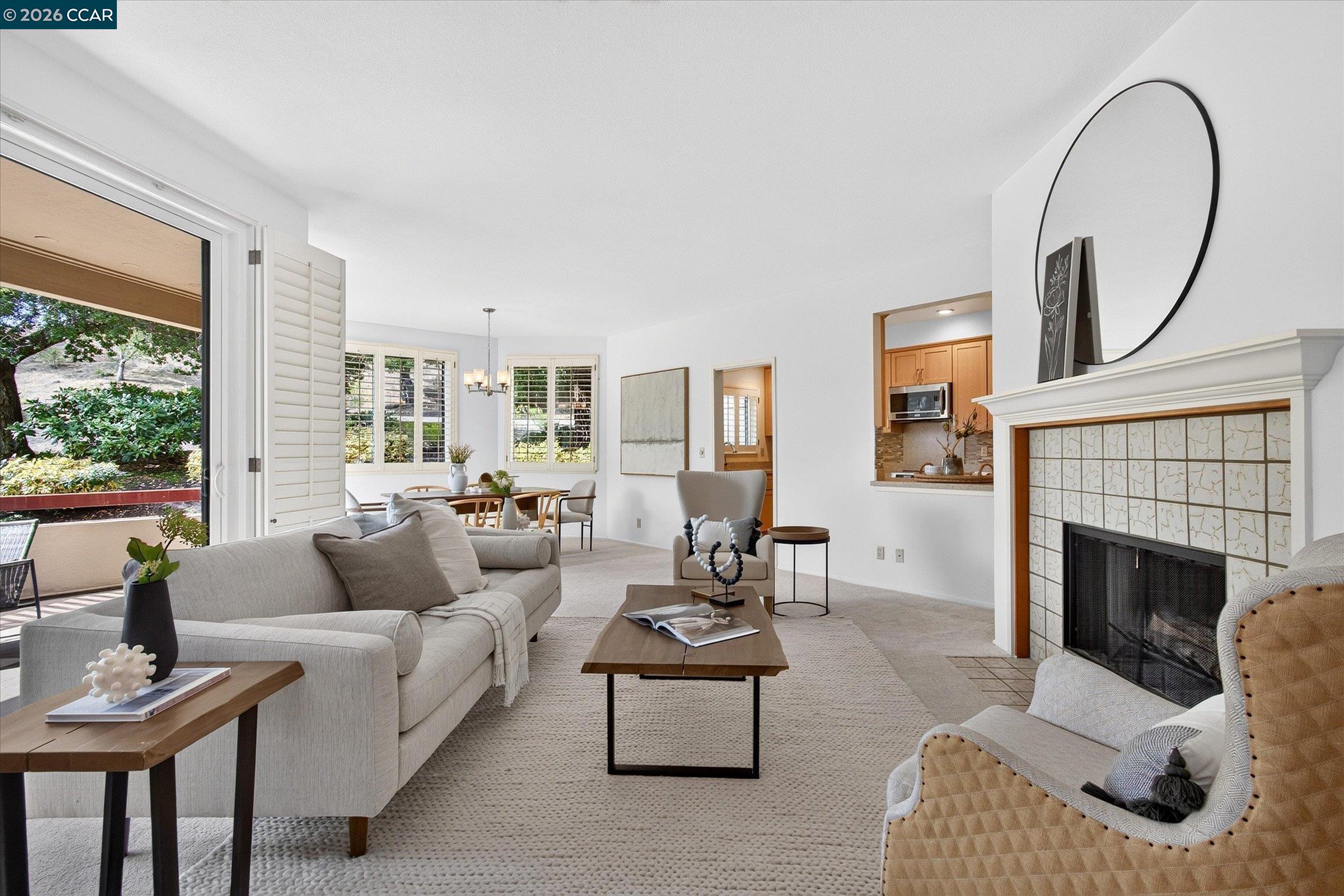 Staged living room with a tiled fireplace, light sofas, and shuttered windows overlooking greenery.