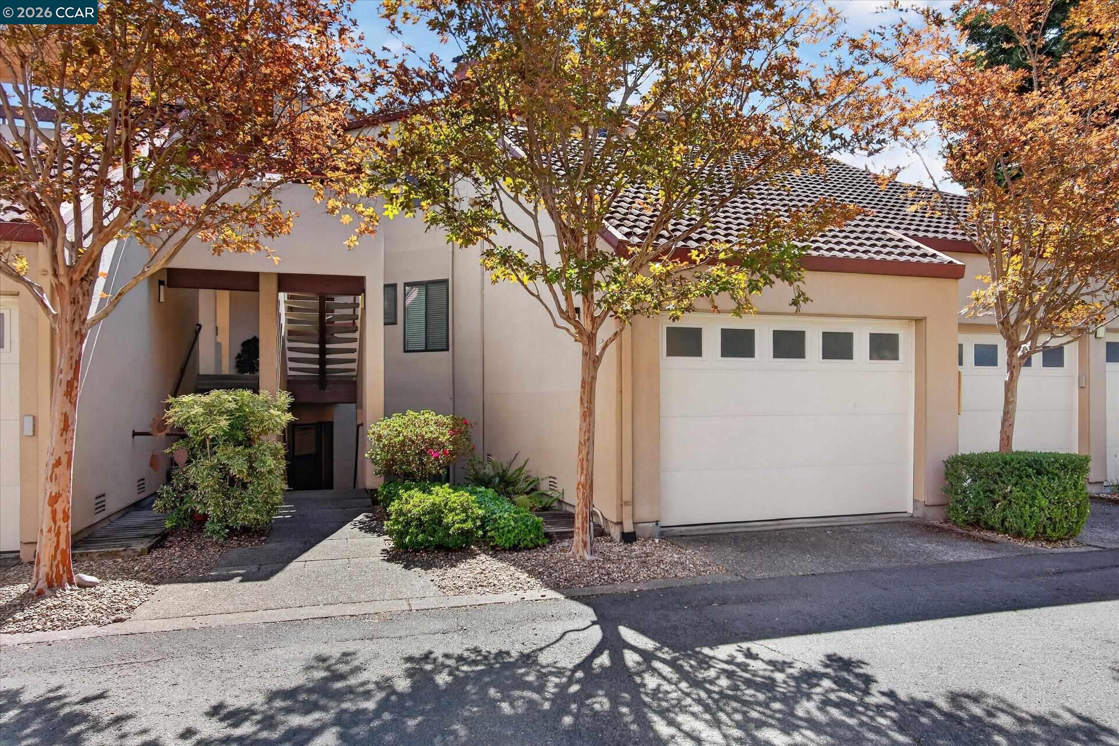 Attached home with tiled roof, white garage door, recessed entrance, and autumn trees.