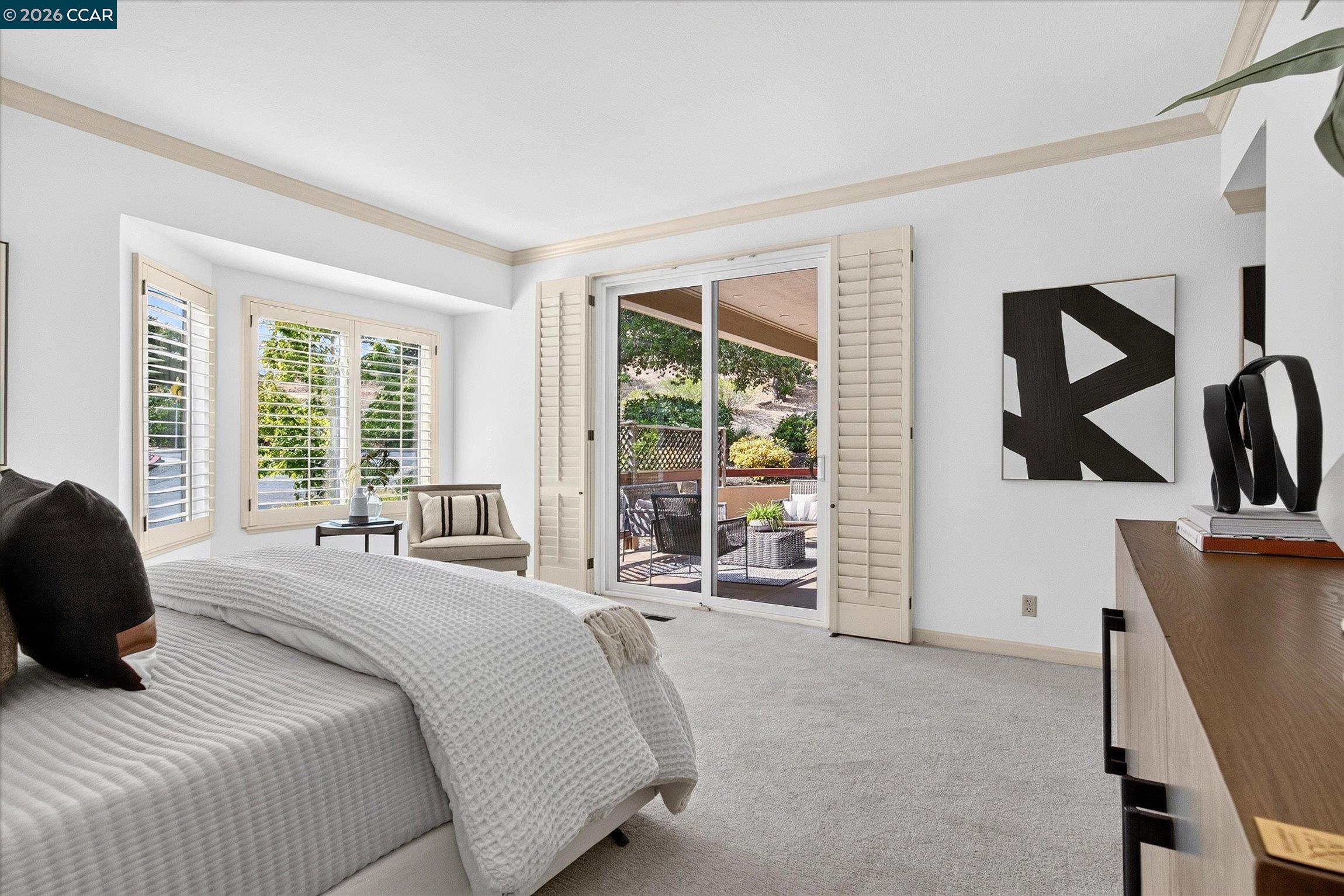 Furnished bedroom with plantation shutters and sliding glass doors opening to a patio.