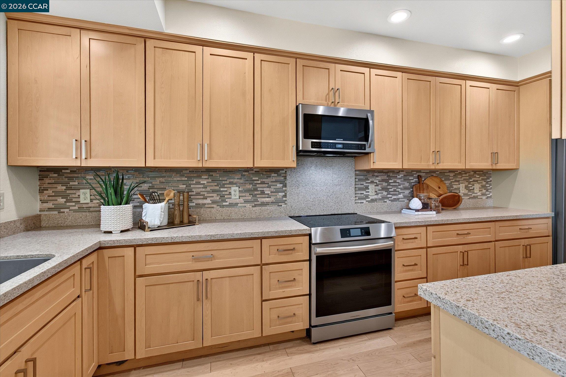 Kitchen with light maple cabinets, granite counters, mosaic backsplash, and stainless steel appliances.