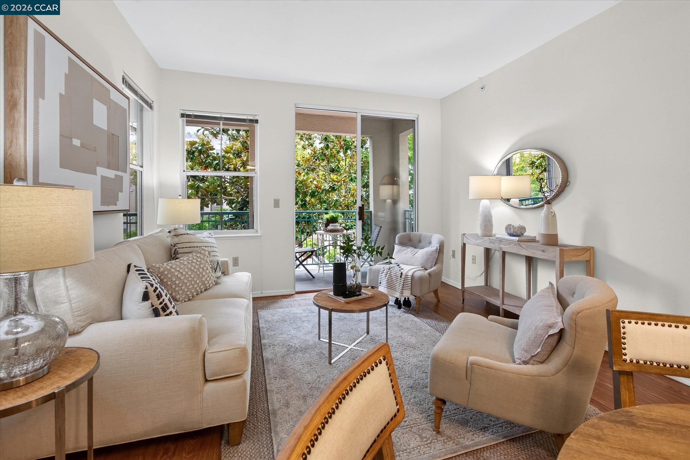 Living room with cream seating and a sliding glass door opening onto a leafy balcony.