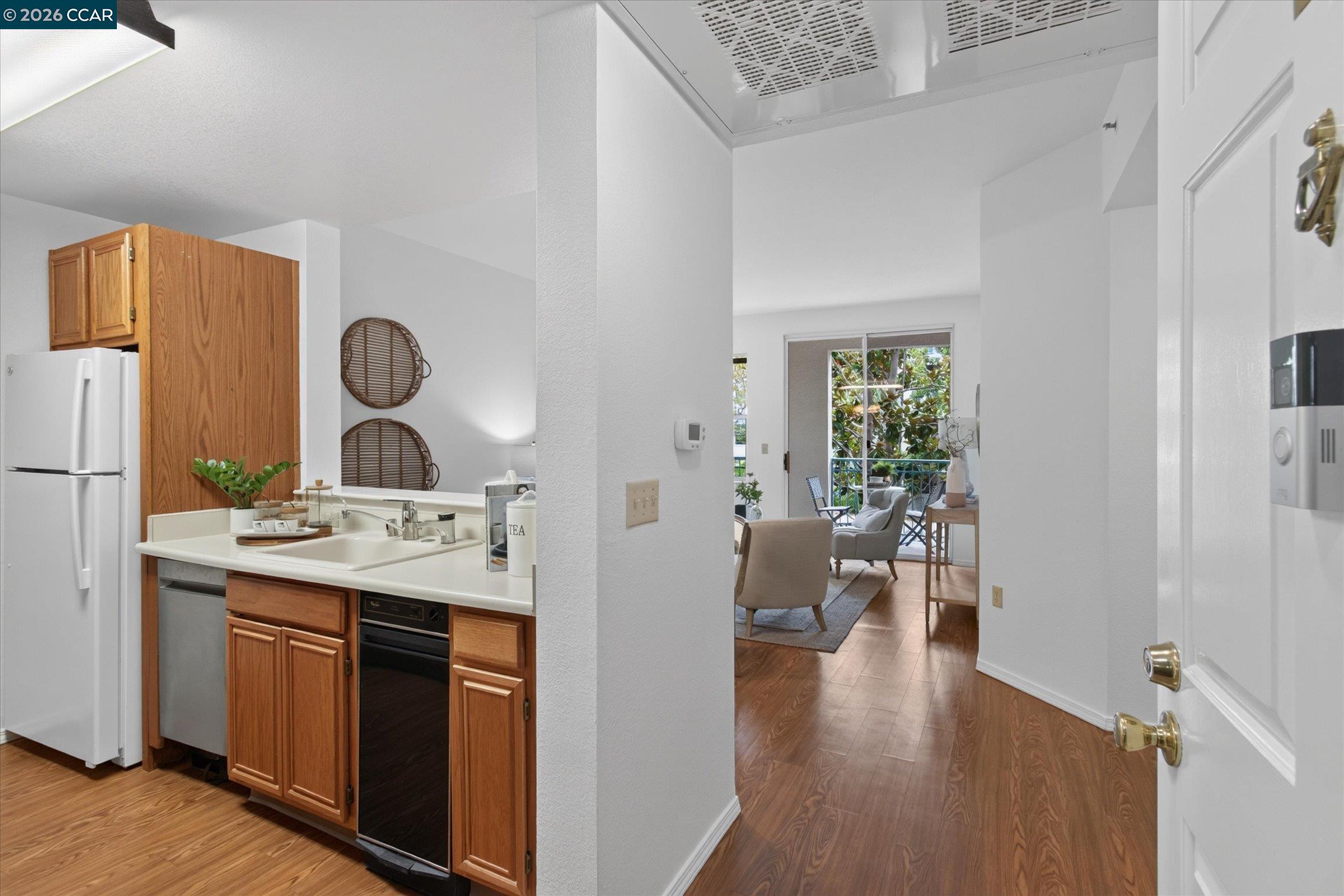 Kitchen with wood cabinets and white appliances opening into a furnished living area.